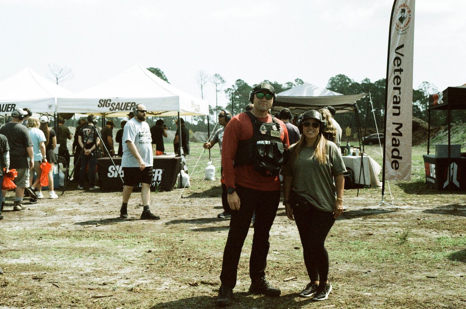 Couple posing together at an outdoor vendor event near a Veteran Made banner on a cloudy day.