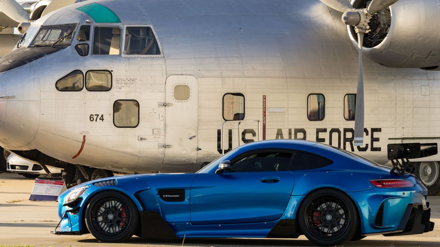 Vintage military aircraft and classic sports cars on display at an aviation museum.
