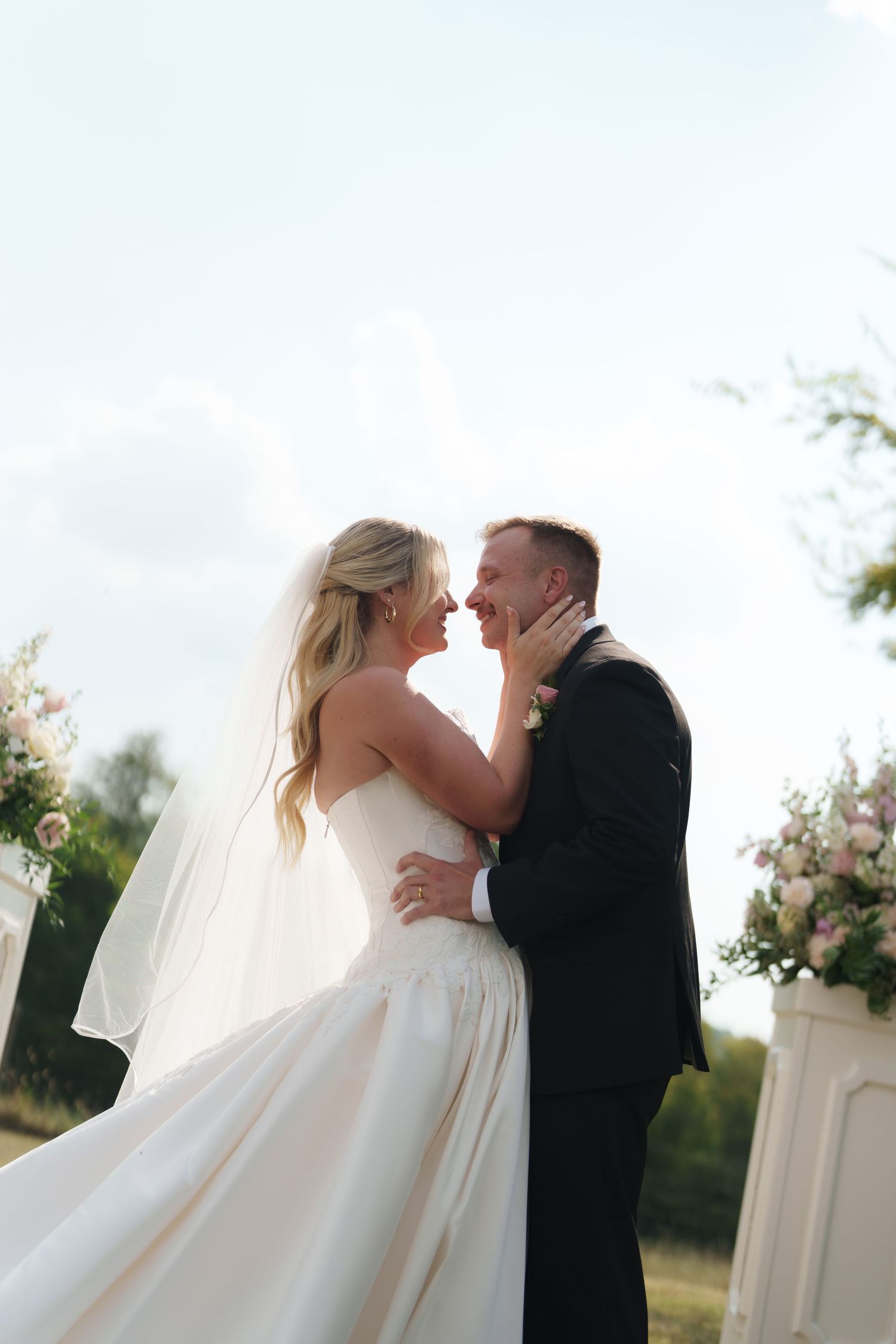 Bride and groom share a romantic moment outdoors, with the bride in a white gown and veil, and groom in a black suit.