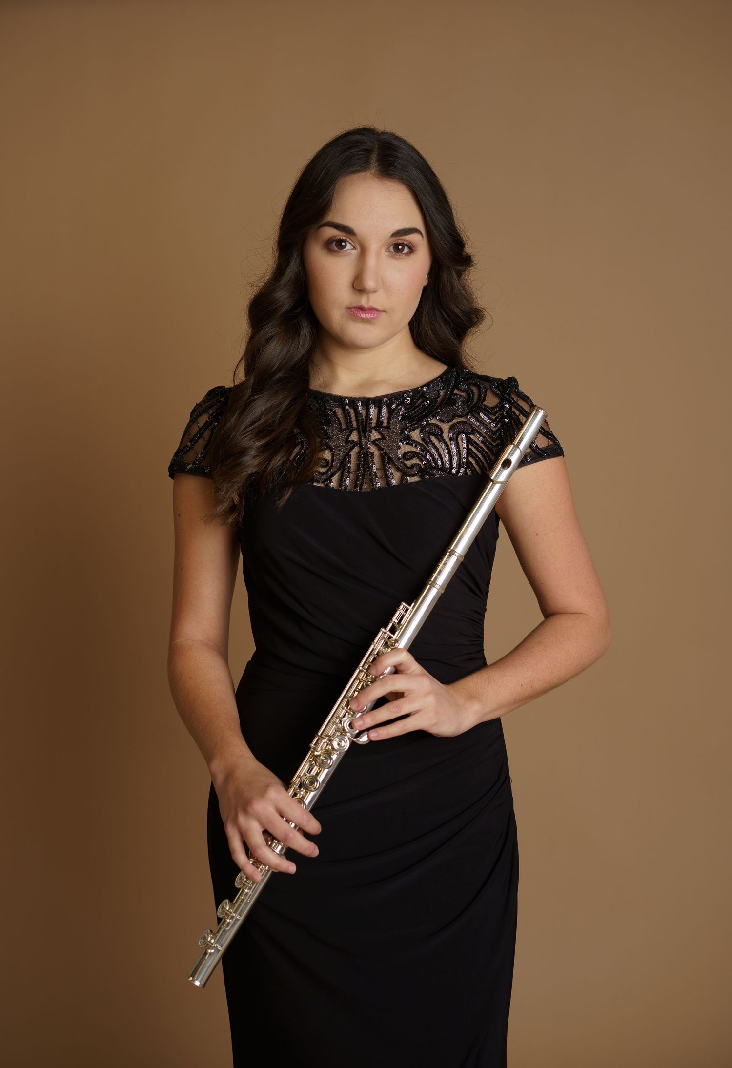 Professional musician in black lace dress poses with flute against brown background.