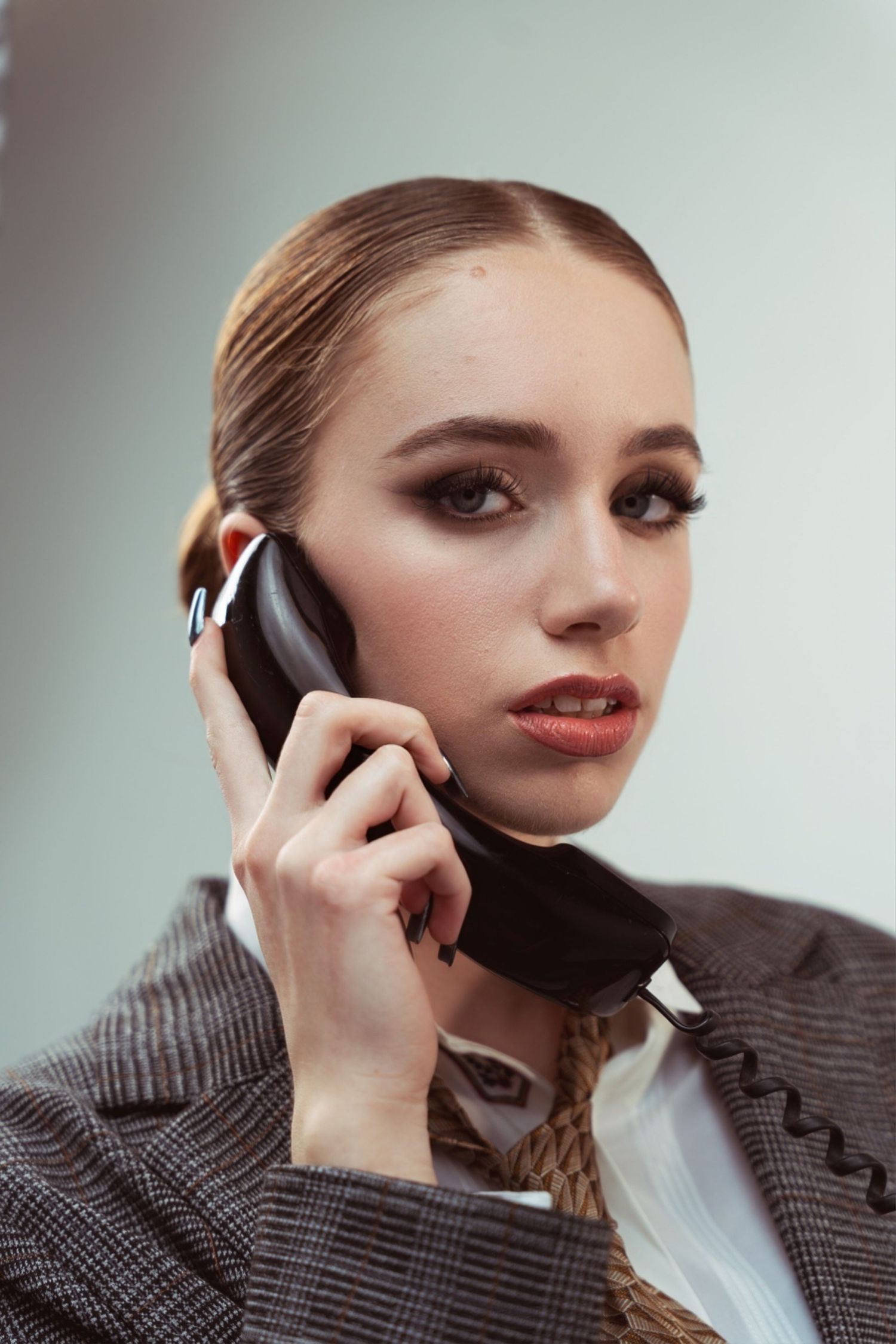 Professional speaking on vintage telephone wearing dark blazer and makeup in studio portrait.