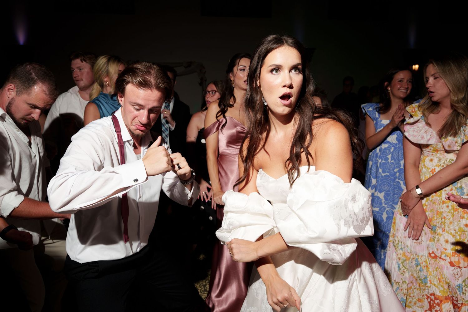 A candid reception moment shows guests dancing and celebrating with energy in a darkened venue.