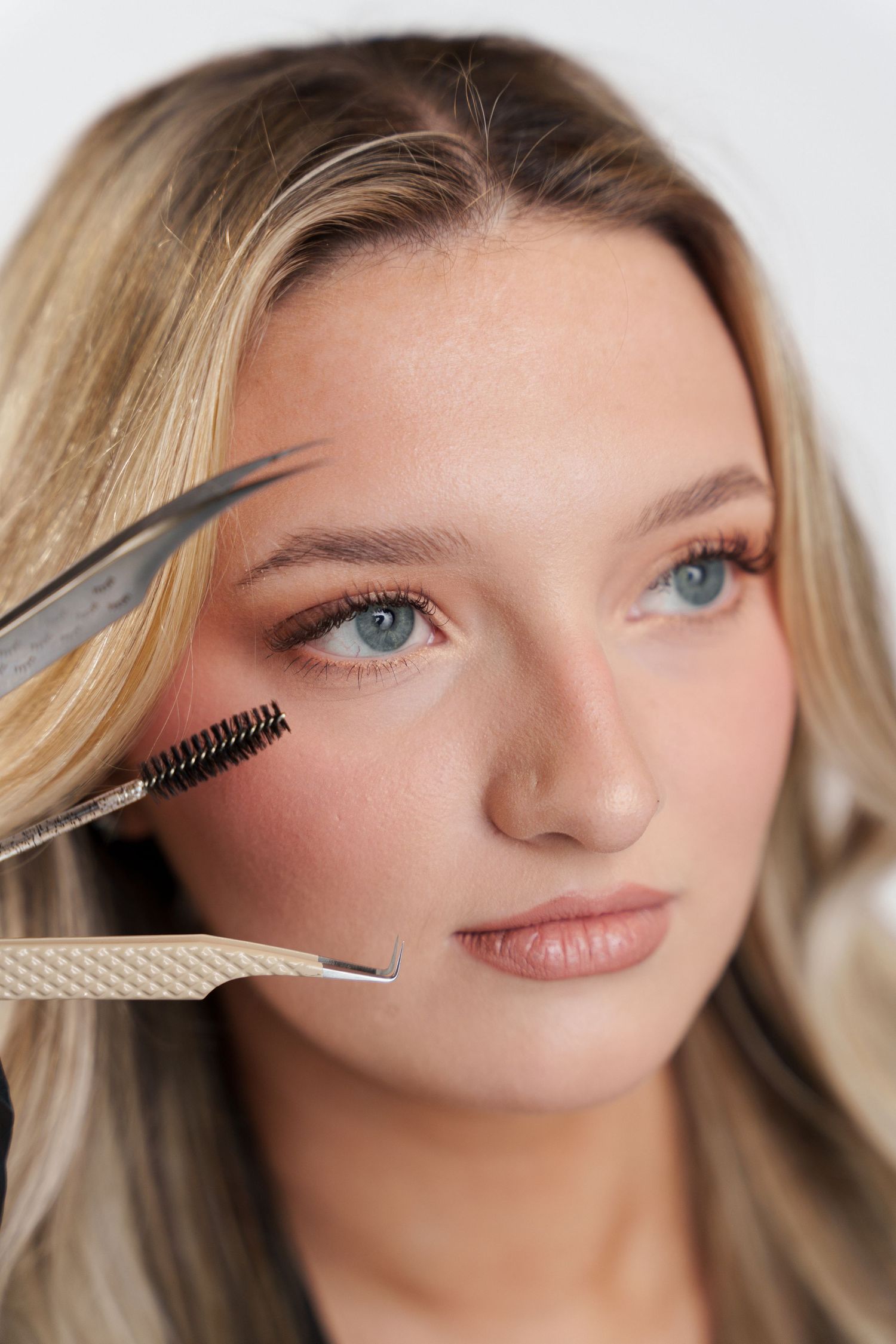Close up of brow grooming with tweezers and brush tools.