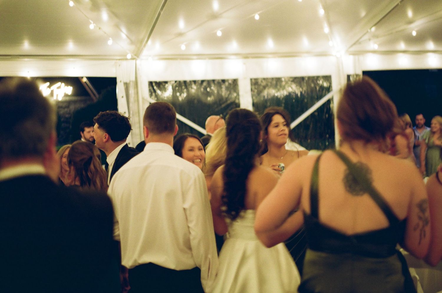 Guests dancing under string lights at an elegant outdoor wedding reception tent at night.