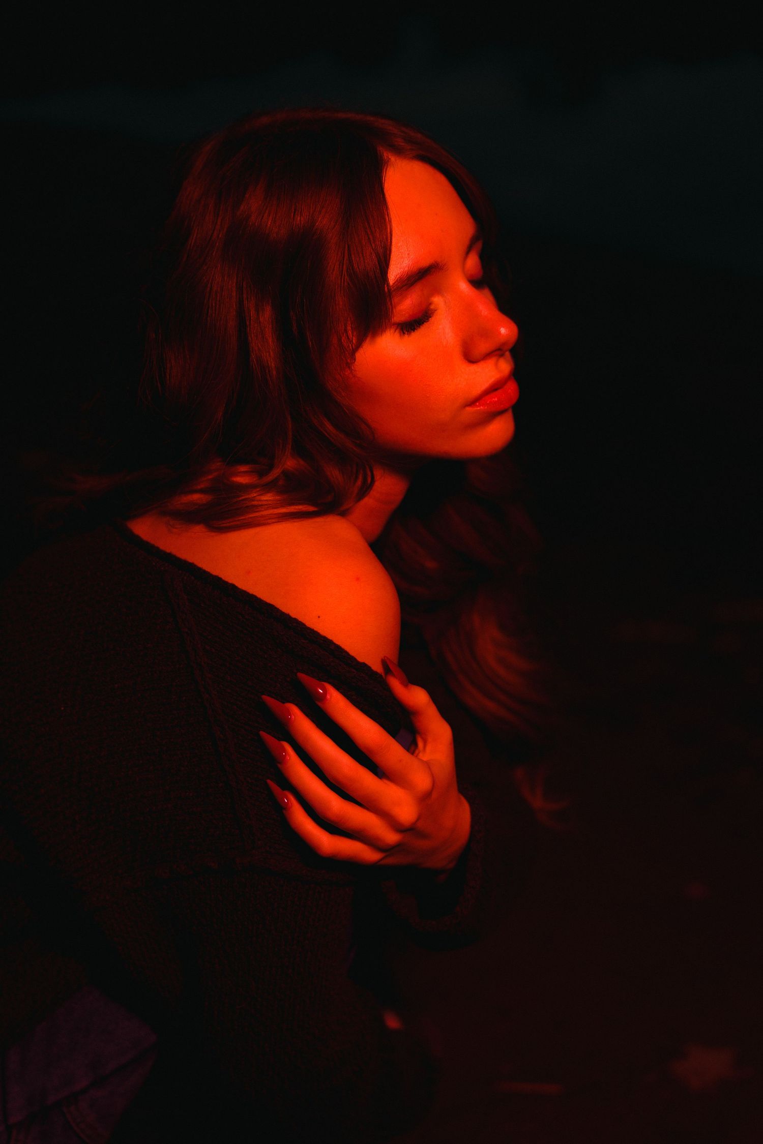 Artistic portrait bathed in moody red lighting shows a contemplative moment against dark background.