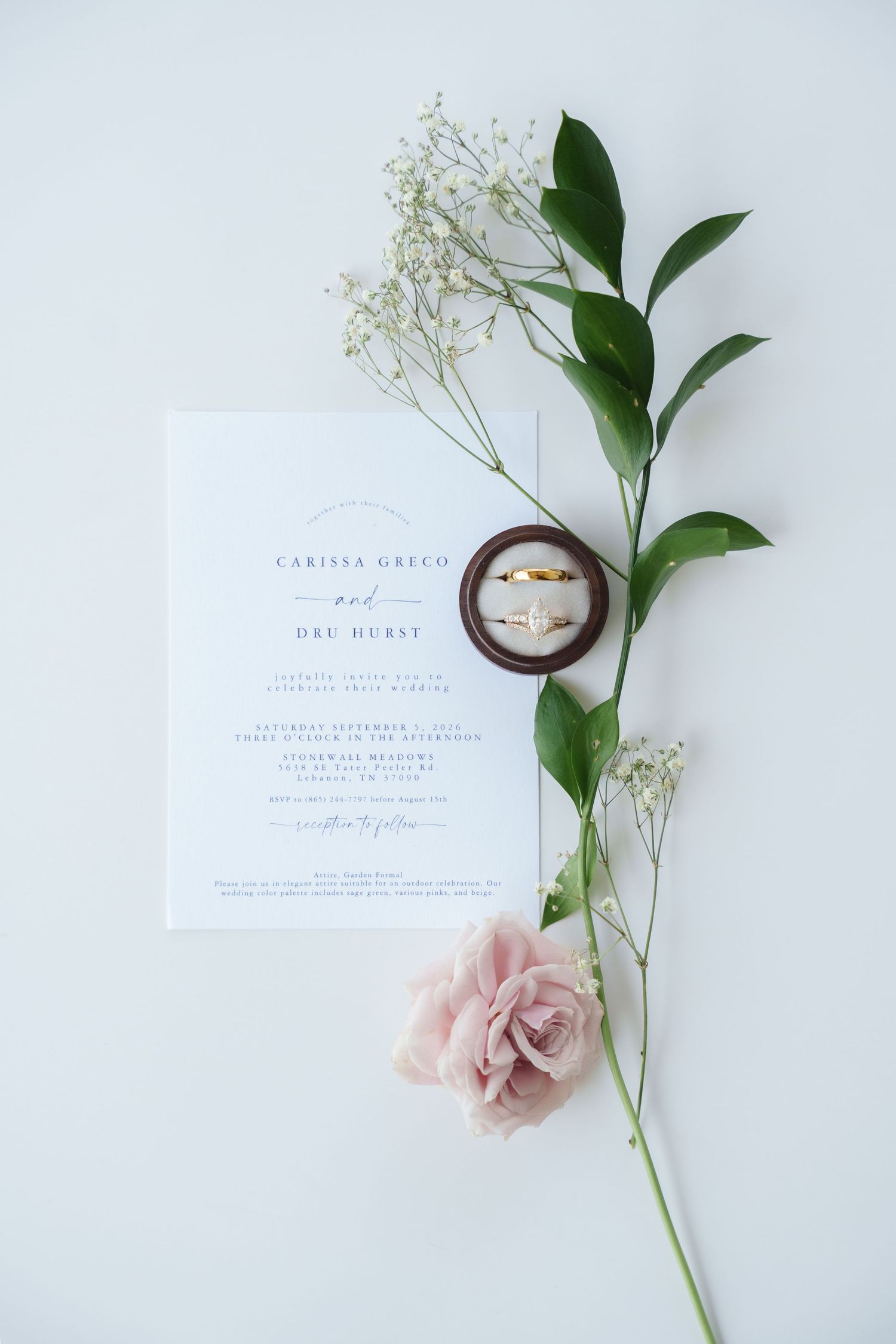 Elegant wedding invitation with gold rings, pink rose, and baby's breath on white background.