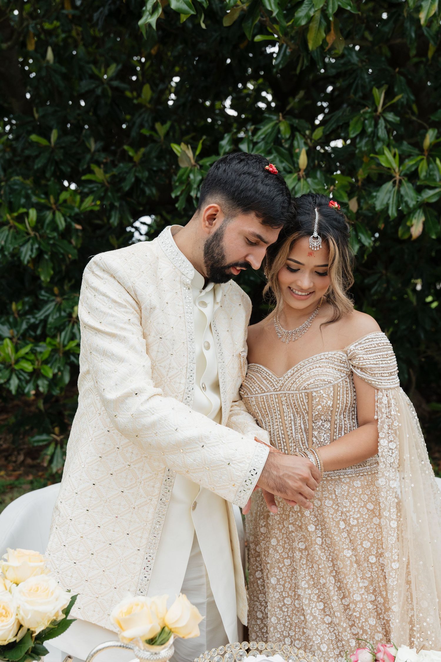 A romantic wedding scene with couple in cream and sparkly outfits standing by magnolia trees.