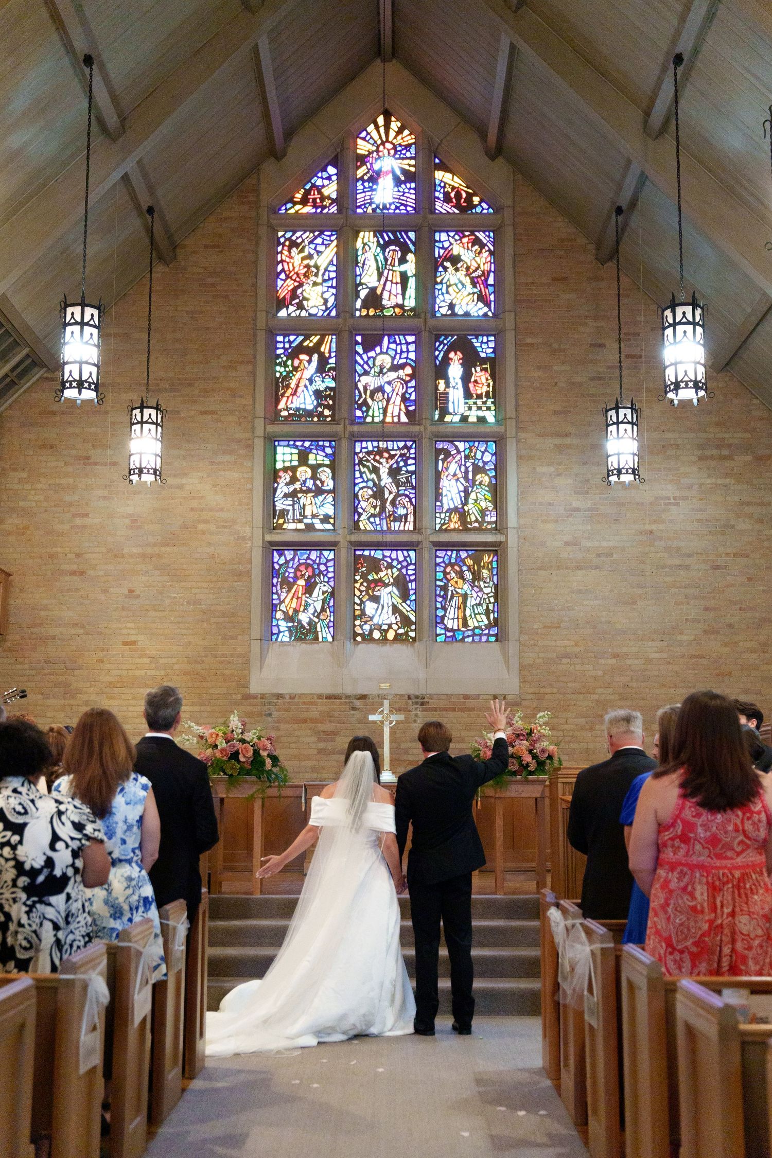 A wedding ceremony takes place in a chapel with beautiful stained glass windows and hanging lanterns illuminating the space.