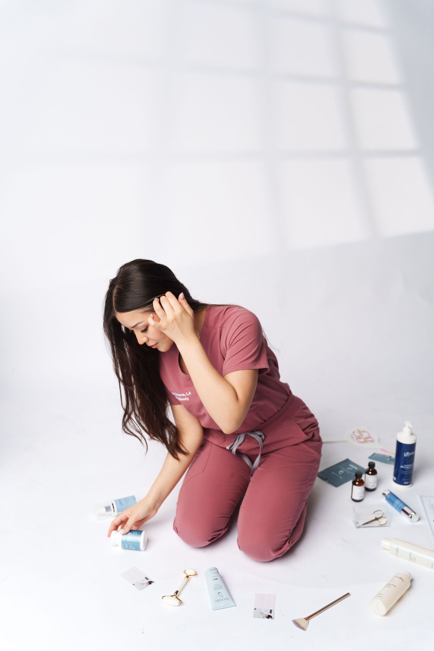 Healthcare worker in pink scrubs kneels on floor surrounded by scattered medical supplies and appears distressed.