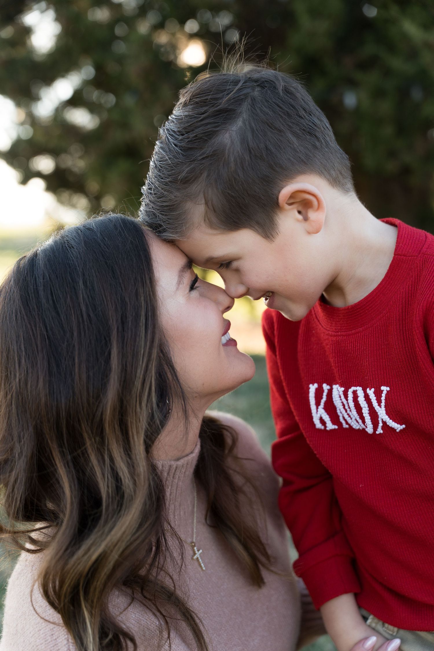 A mother and young boy named Knox share a tender nose-to-nose moment outdoors.