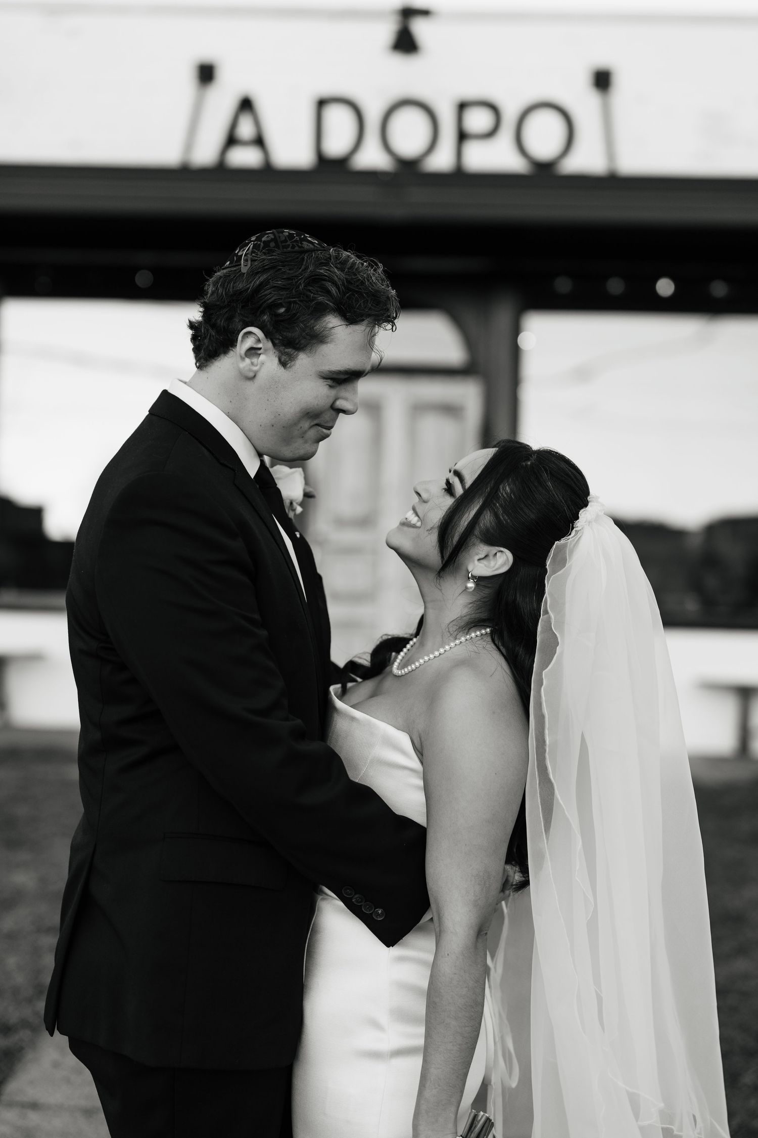 Black and white photo of bride and groom sharing a romantic moment in front of A Dopo sign.