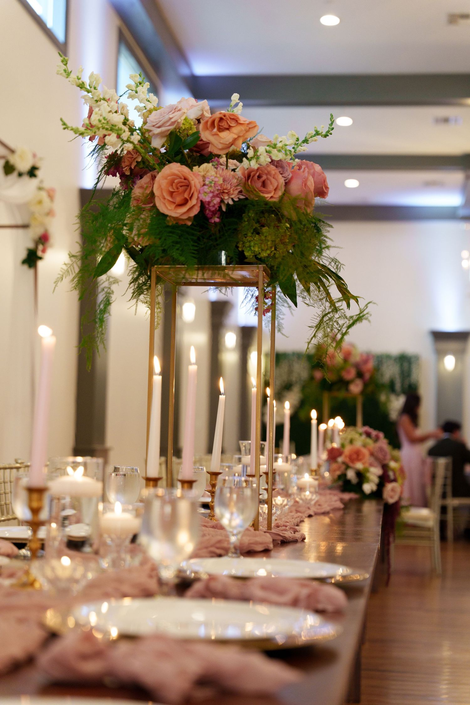 Elegant wedding reception tables with tall floral centerpieces in pink and white with glowing candlelight.