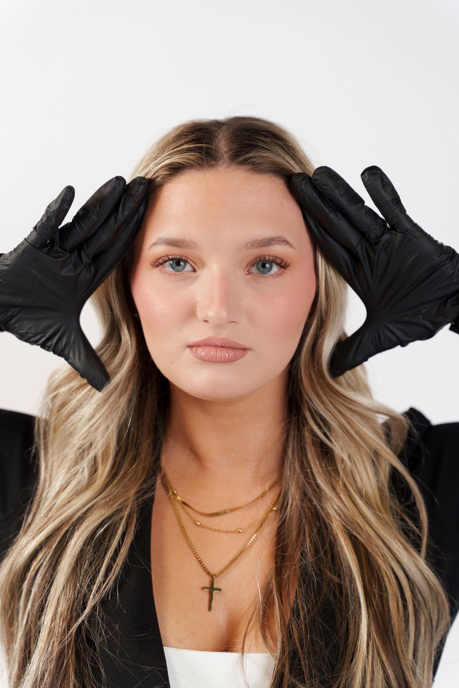 Stylish portrait with black gloves, layered necklaces and blonde balayage hair against white backdrop.