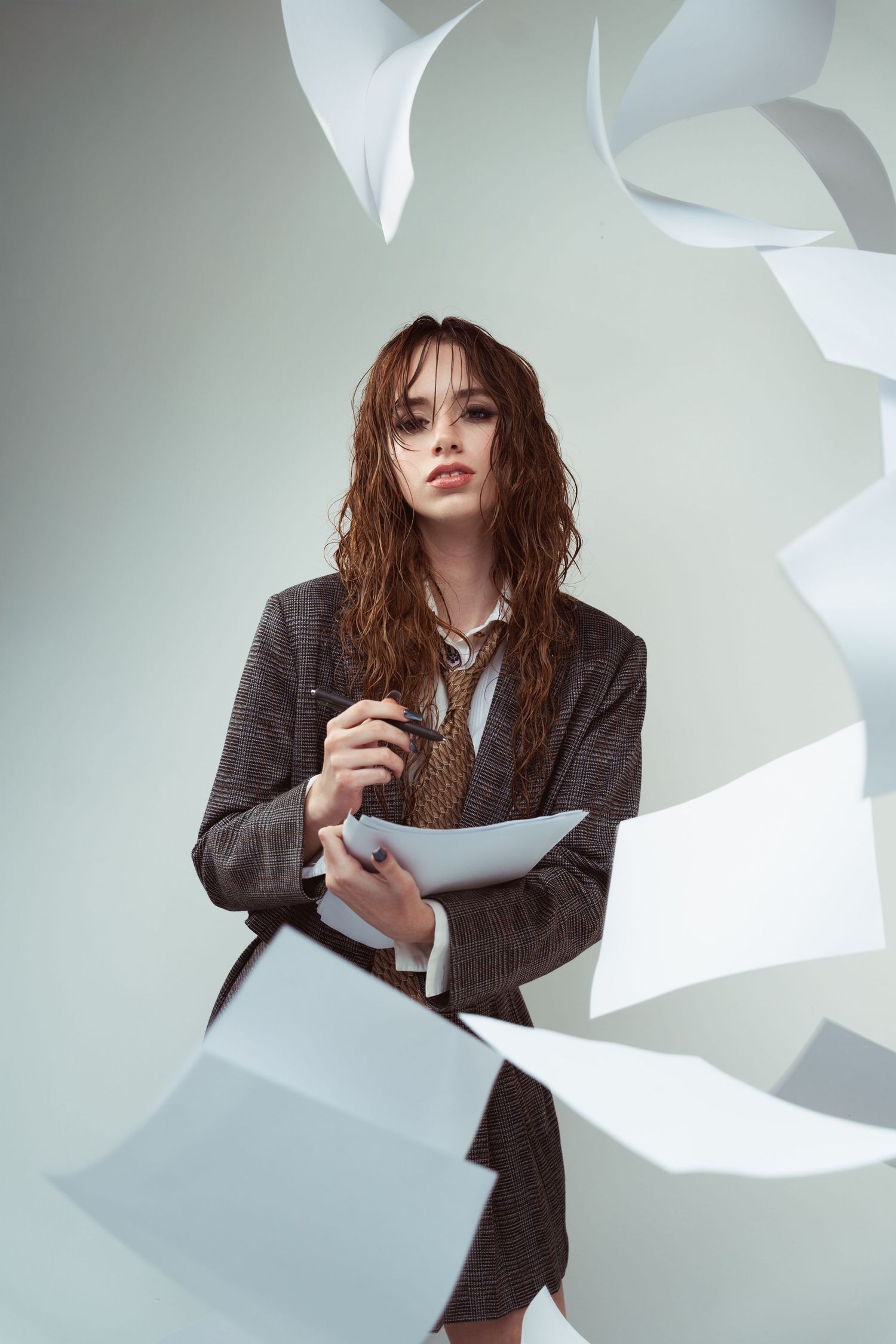 Fashion photo series showing a model in a gray blazer posing with large white paper shapes against a light backdrop.