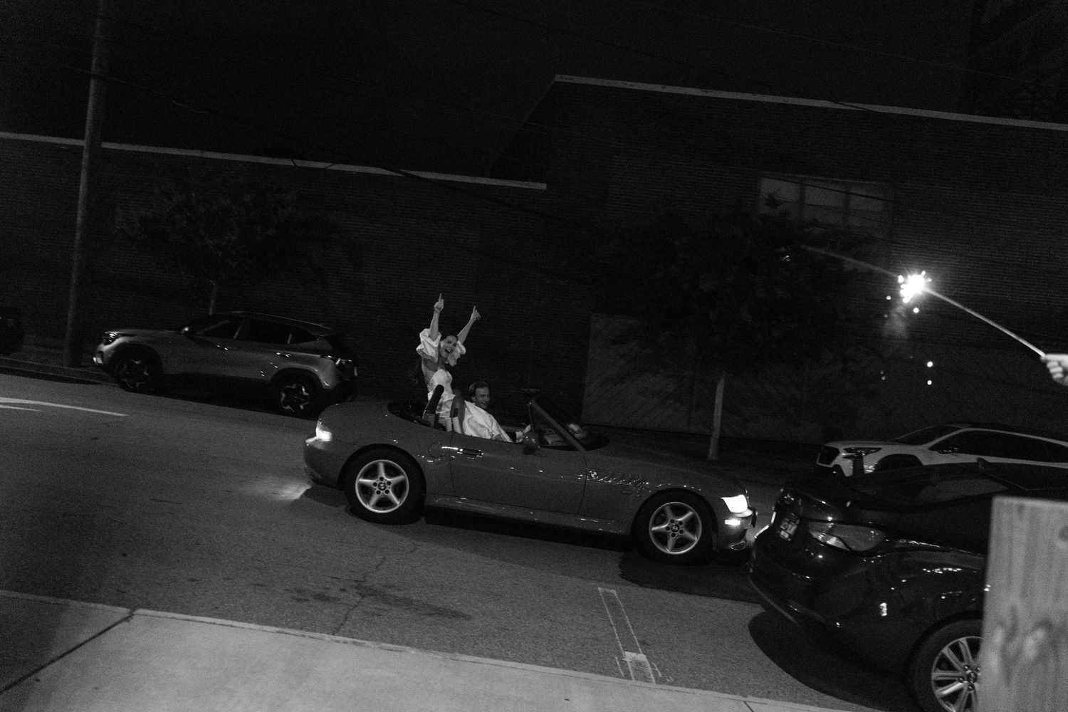 Black and white nighttime photograph of parked cars in a dimly lit parking lot.