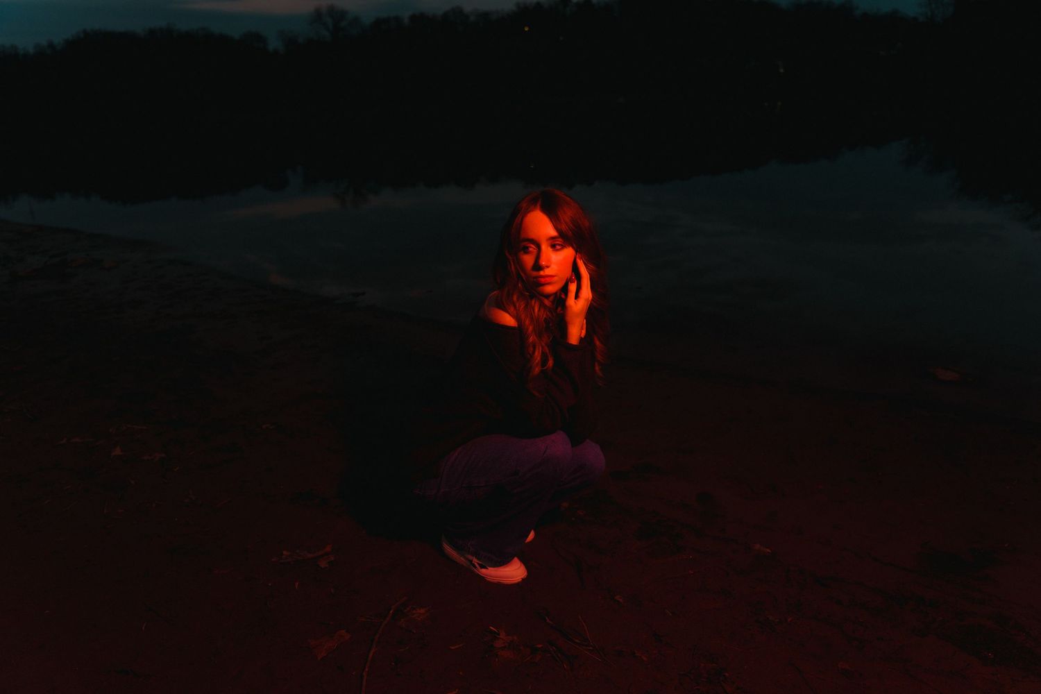 A person crouches in darkness illuminated by dramatic red lighting creating a moody outdoor scene.