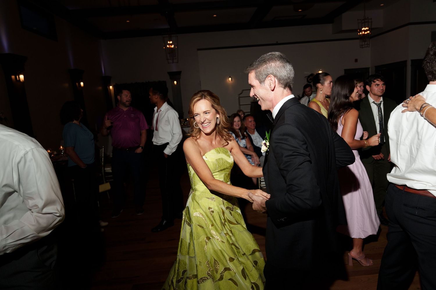 A person in a lime green dress and their dance partner move gracefully on a darkened dance floor at an event.