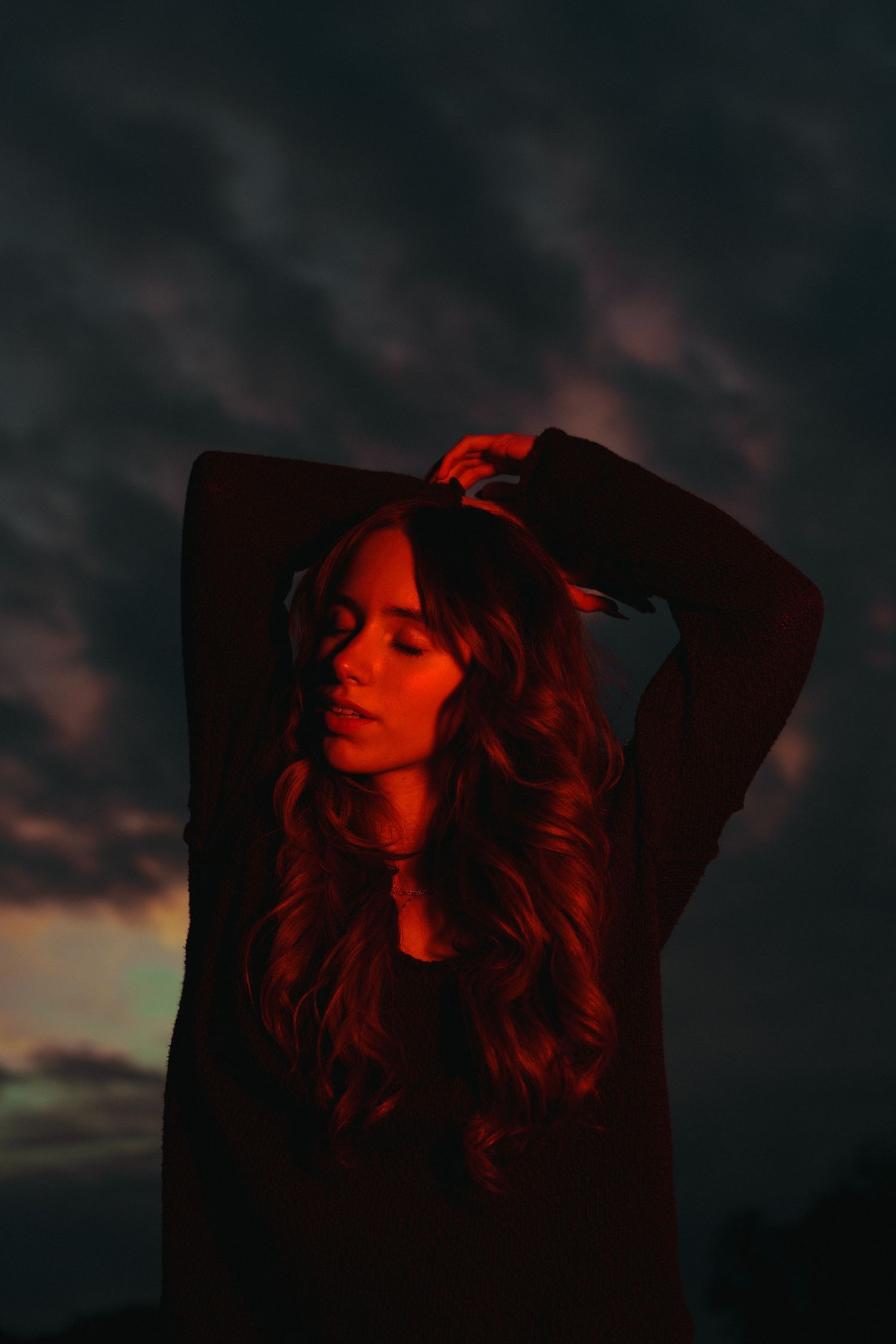 Silhouette in moody sunset with dark clouds and dramatic red lighting creating atmospheric portrait.