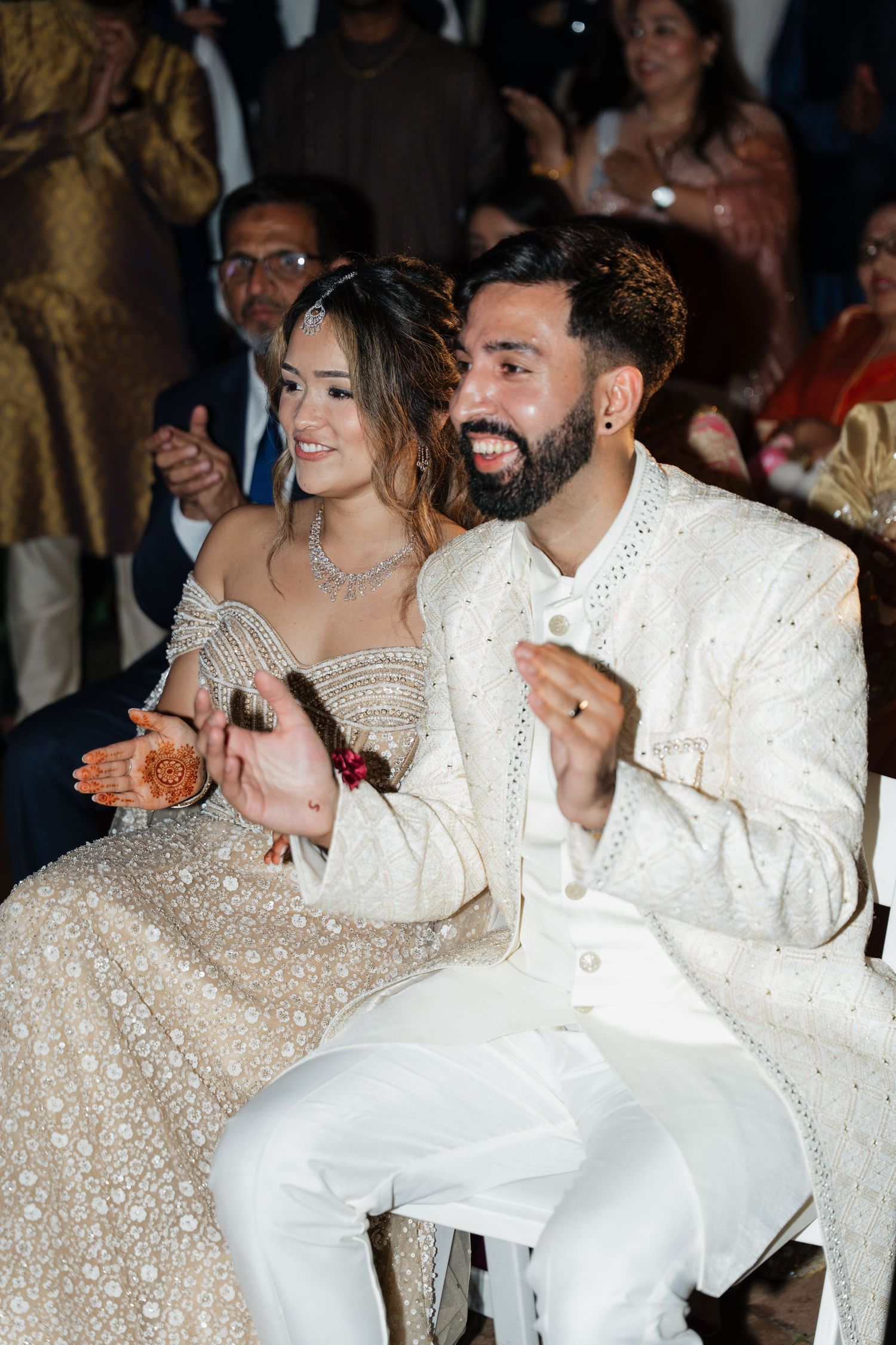 Wedding couple shares joyful moments during reception while wearing elegant matching white outfits.