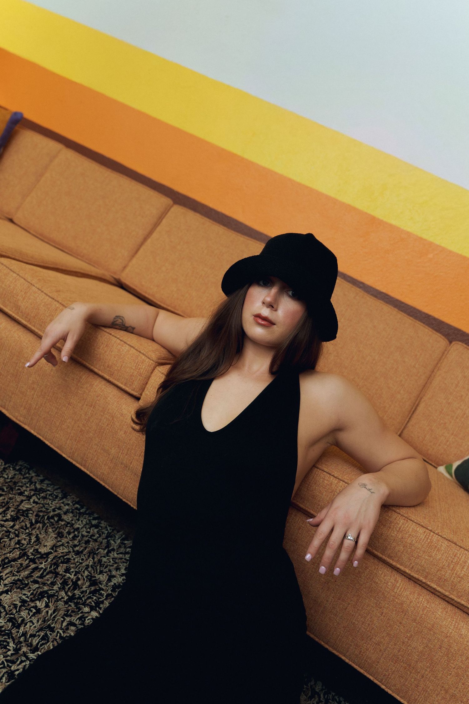 A artistically cropped fashion photo against an orange wall shows someone in a black hat creating dramatic shadows.