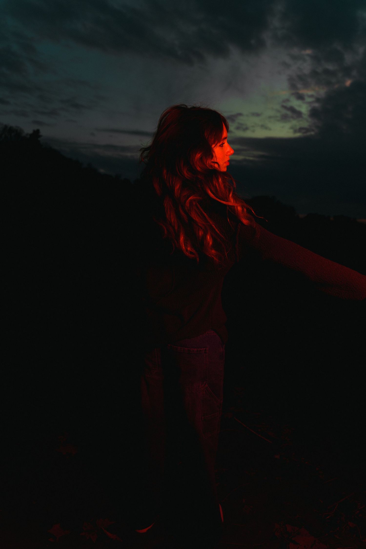 Silhouetted figure stands against dramatic twilight sky illuminated by red light.