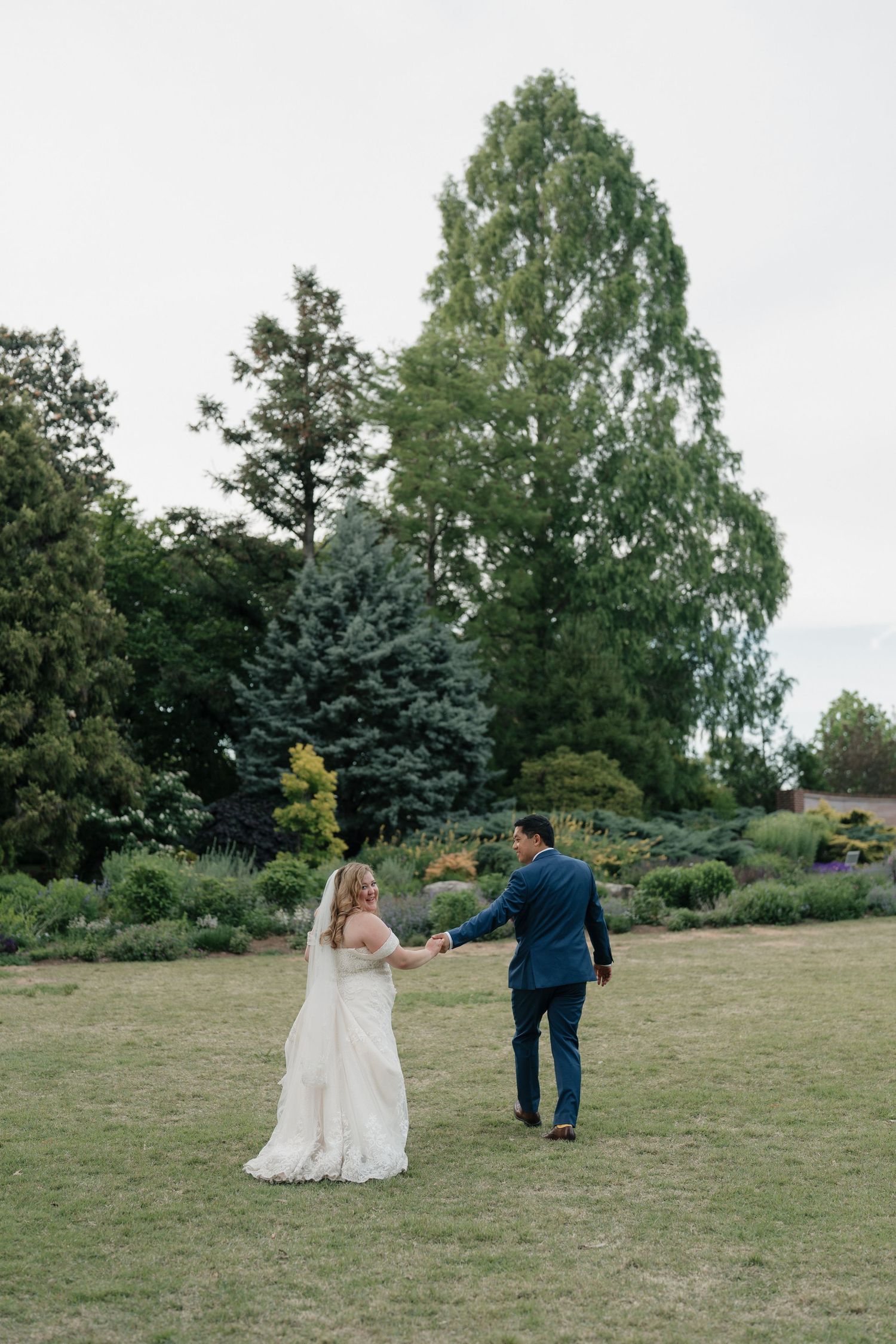 Bride and groom holding hands walking through a lush garden on their wedding day.