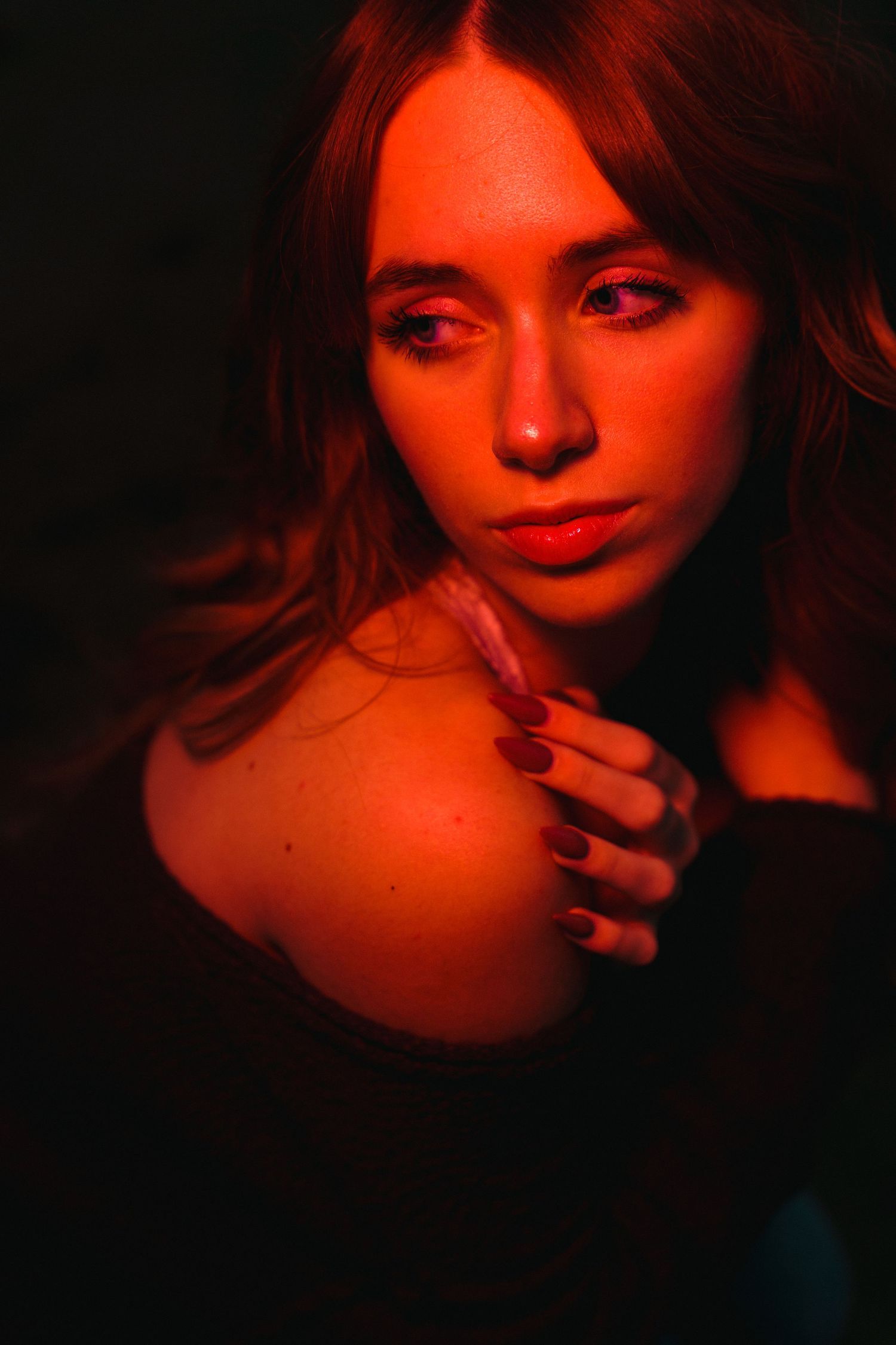 Dramatic portrait in red lighting with dark shadows showing ethereal beauty and long dark hair.
