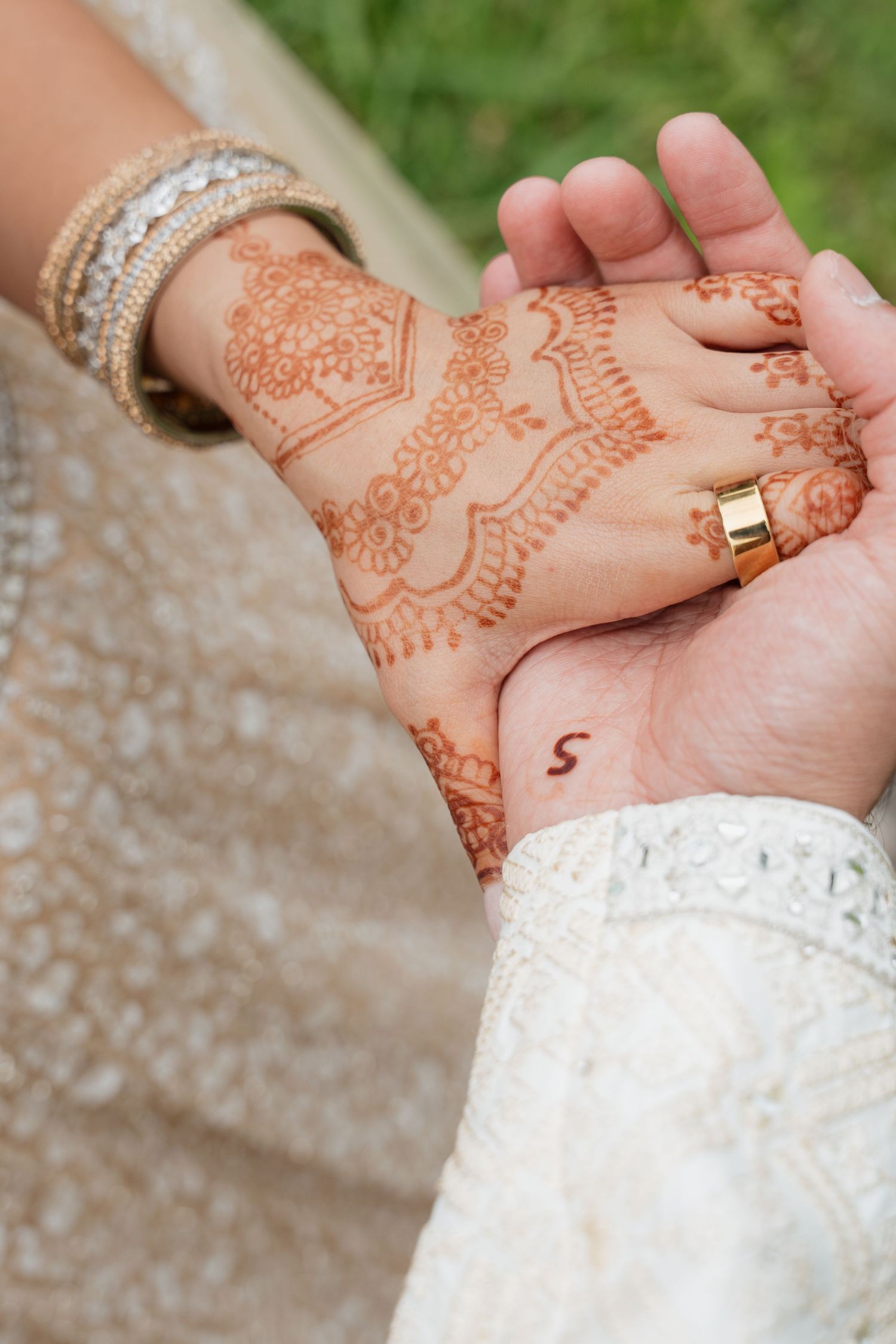 Close-up of intricate henna designs on hands and gold wedding ring details.
