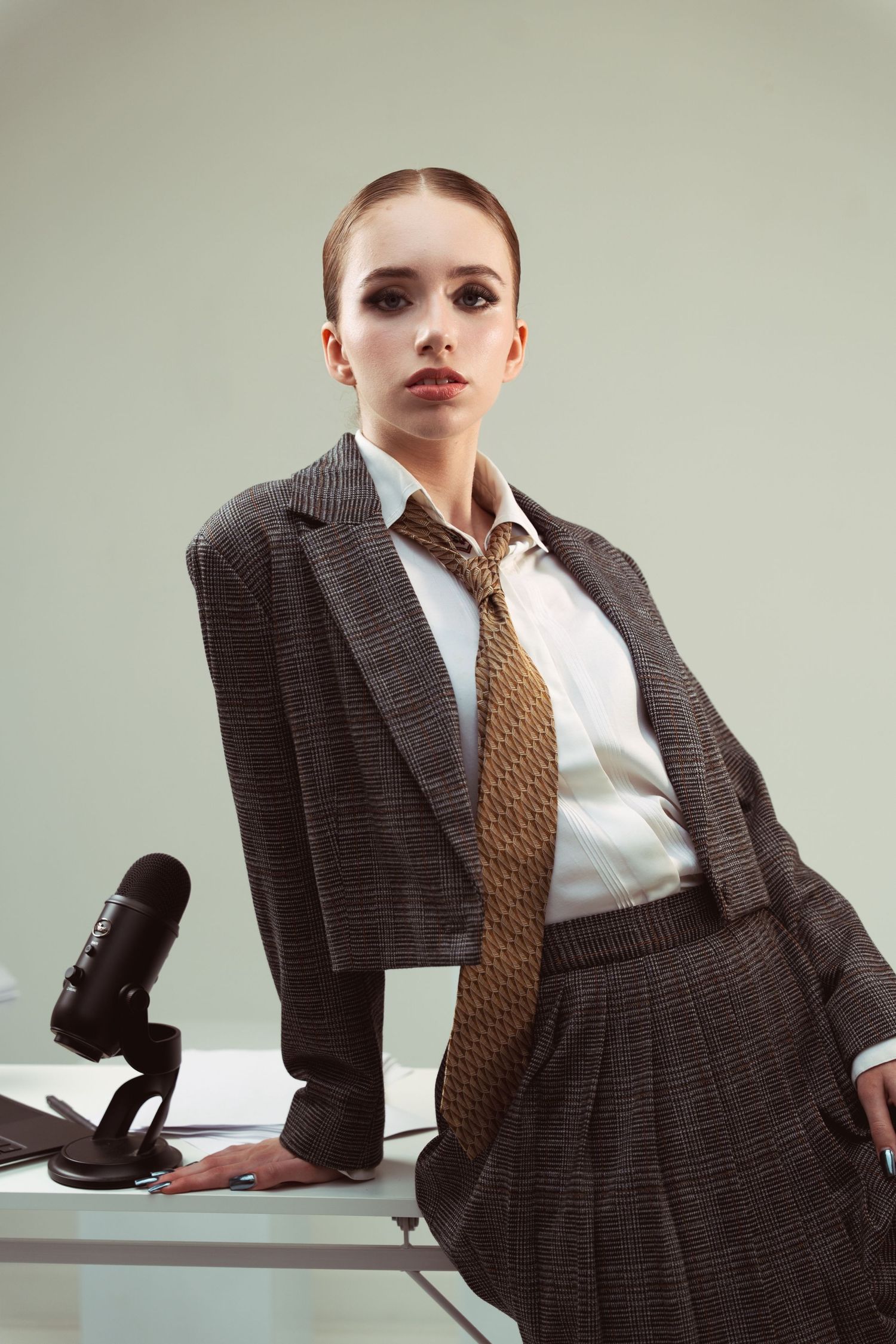 Professional businesswoman in dark suit and tie leaning against desk with retro phone.