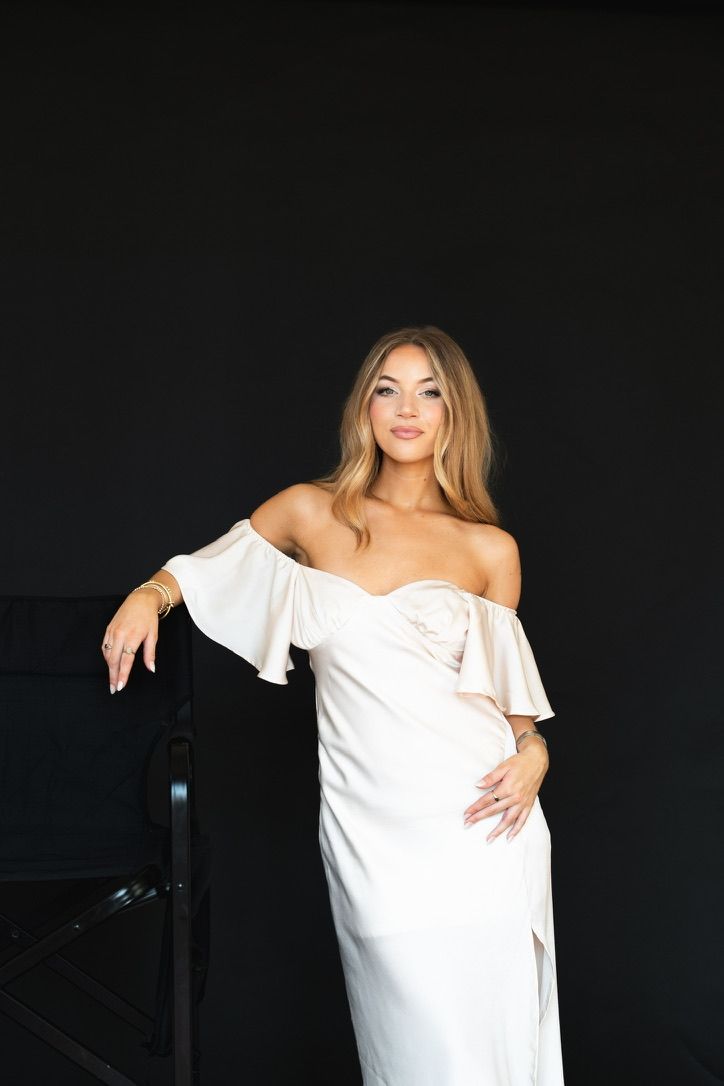 Woman in elegant white off-shoulder gown posing against black background.