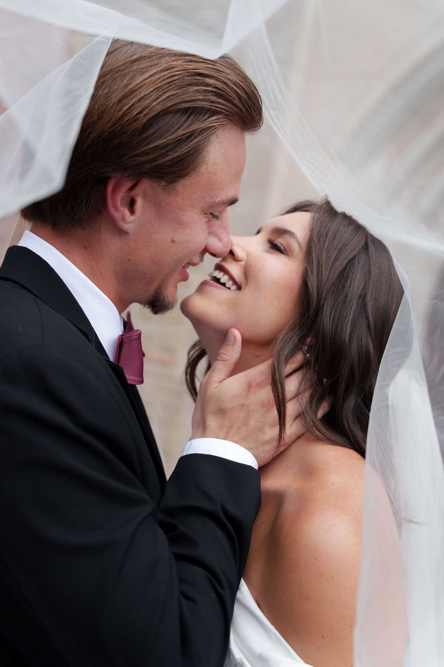 A tender romantic moment captured under a flowing white veil at an elegant wedding celebration.
