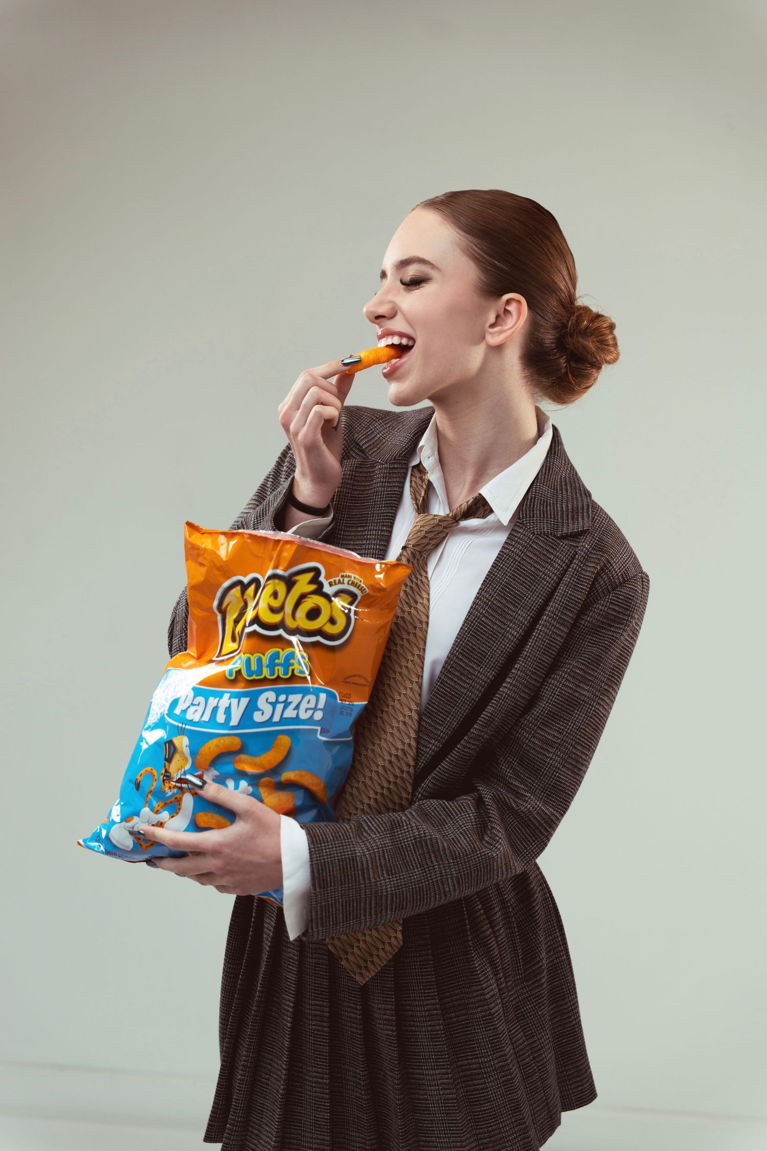 Model in business attire enjoying Cheetos party size snacks during work break.