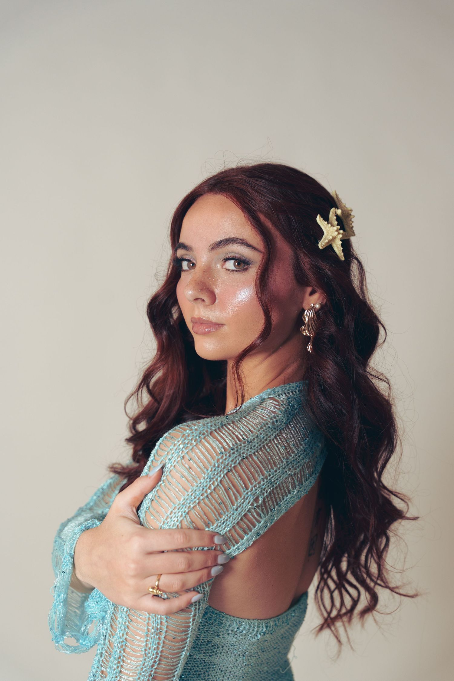 Portrait in turquoise lace dress with flowing dark hair adorned with small floral hair clip against neutral background.
