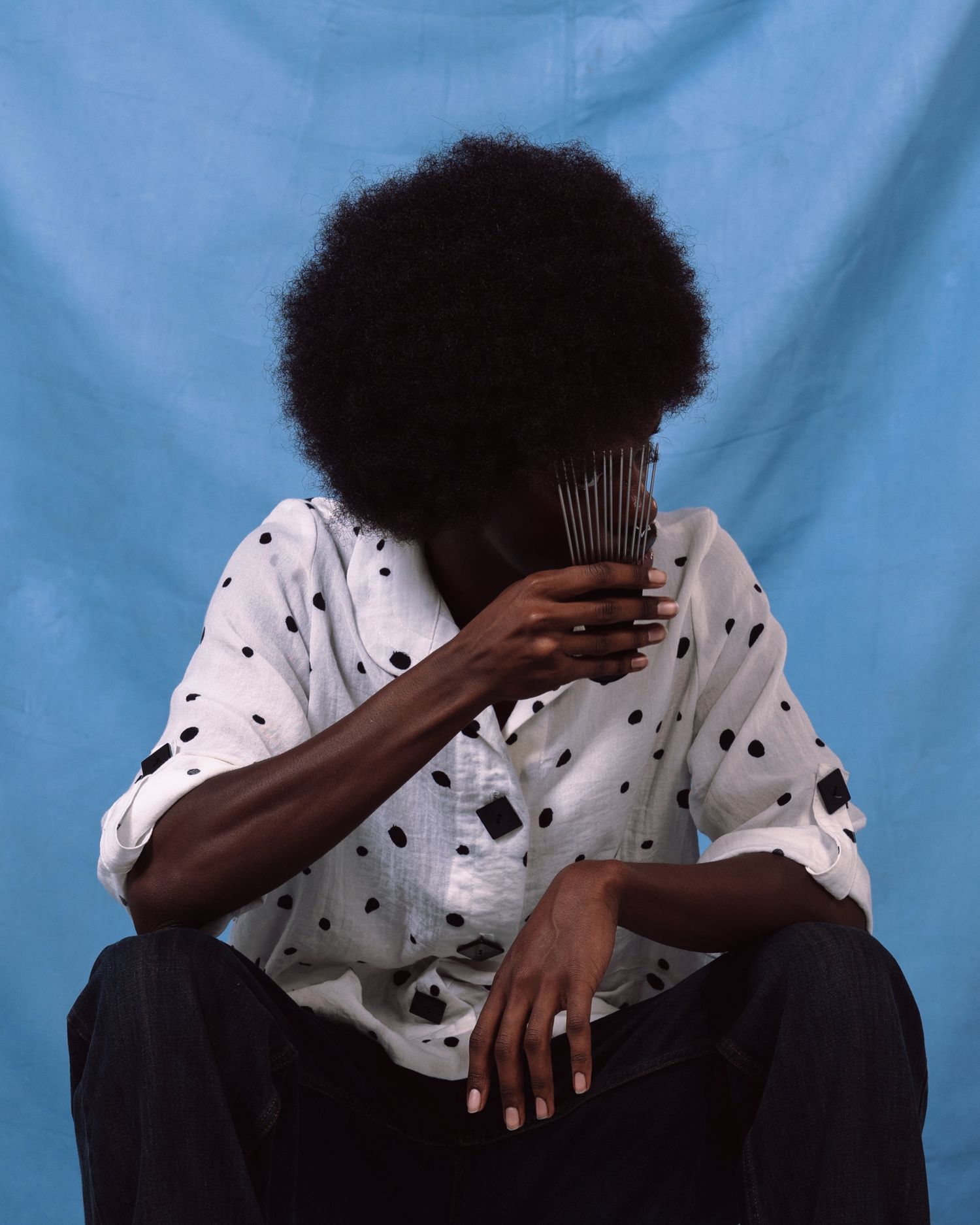 A person wearing a polka dot shirt sits against a light blue background covering their face in a series of emotive poses.
