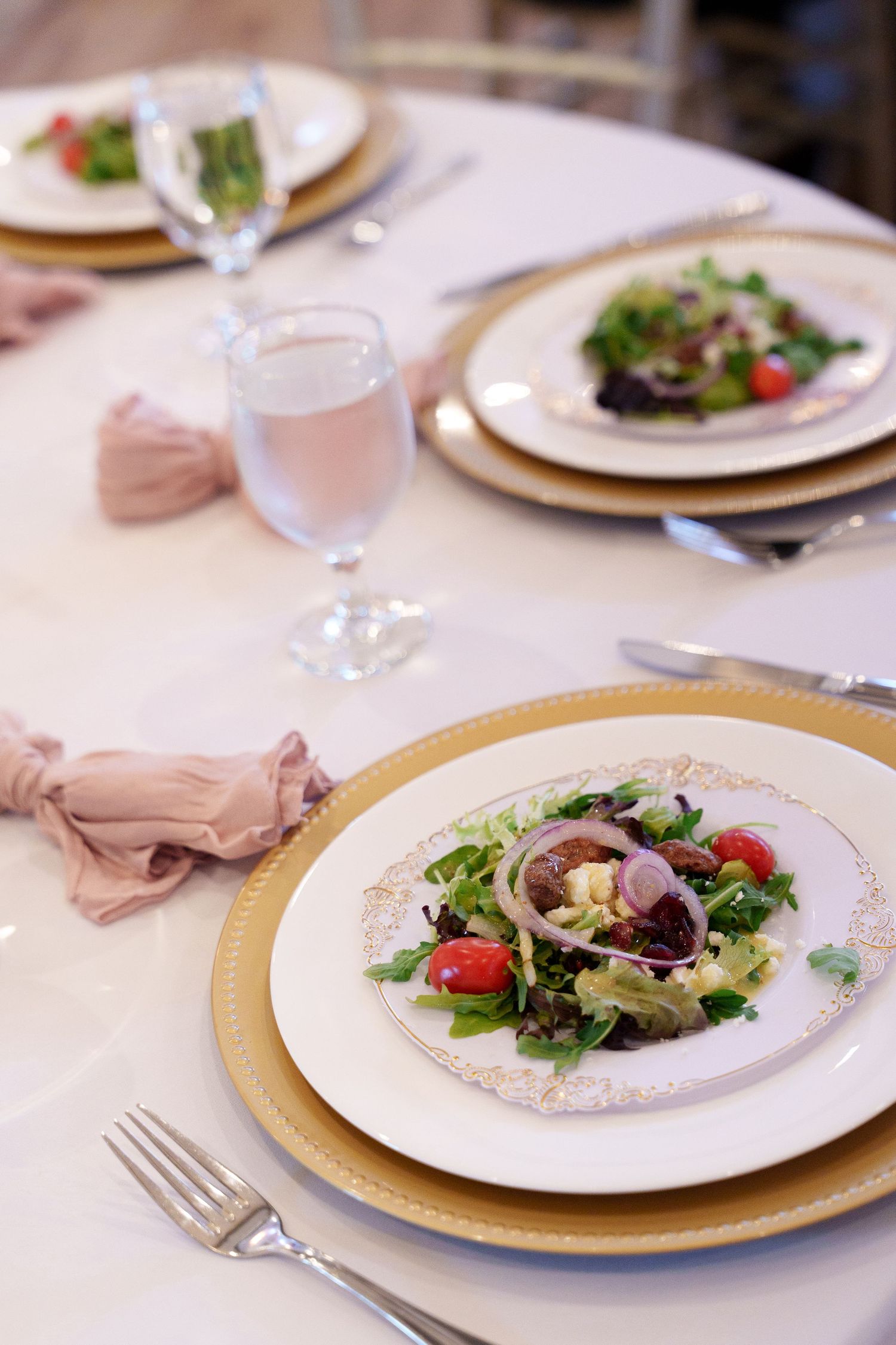 Wedding reception place settings with gold chargers, fine china, and fresh garden salads.