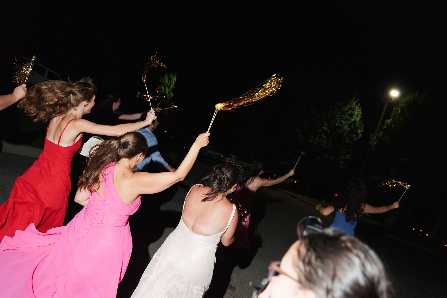 Wedding guests in formal attire wave sparklers at an outdoor nighttime celebration.