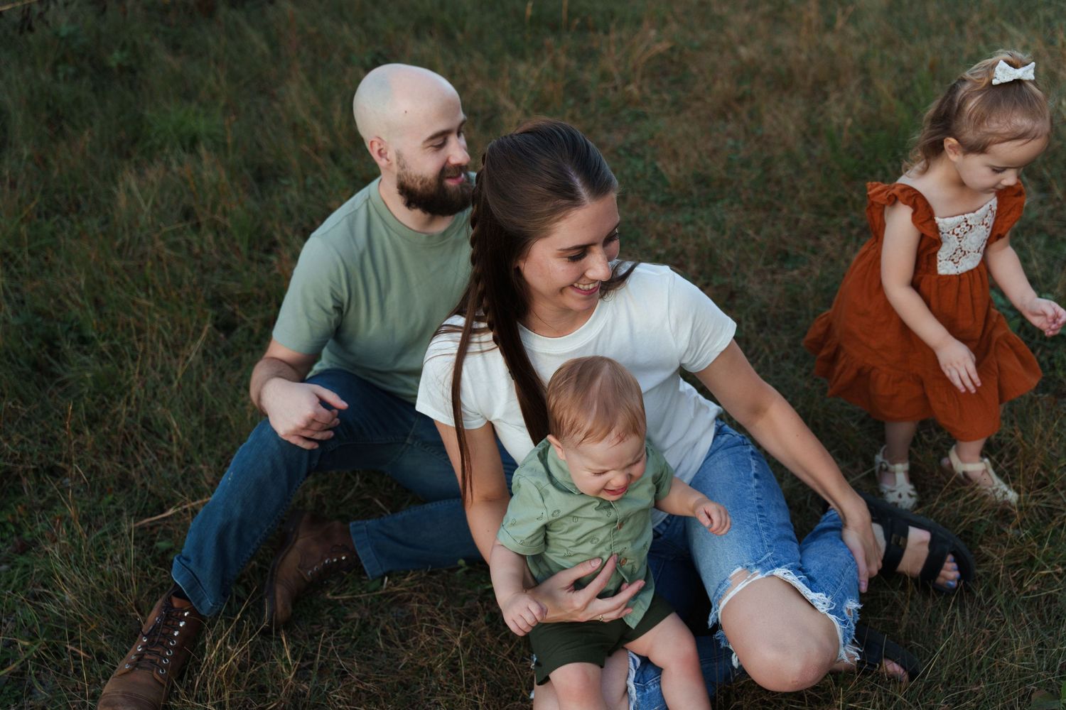 A family sits together on grassy ground during an outdoor photo session at sunset.