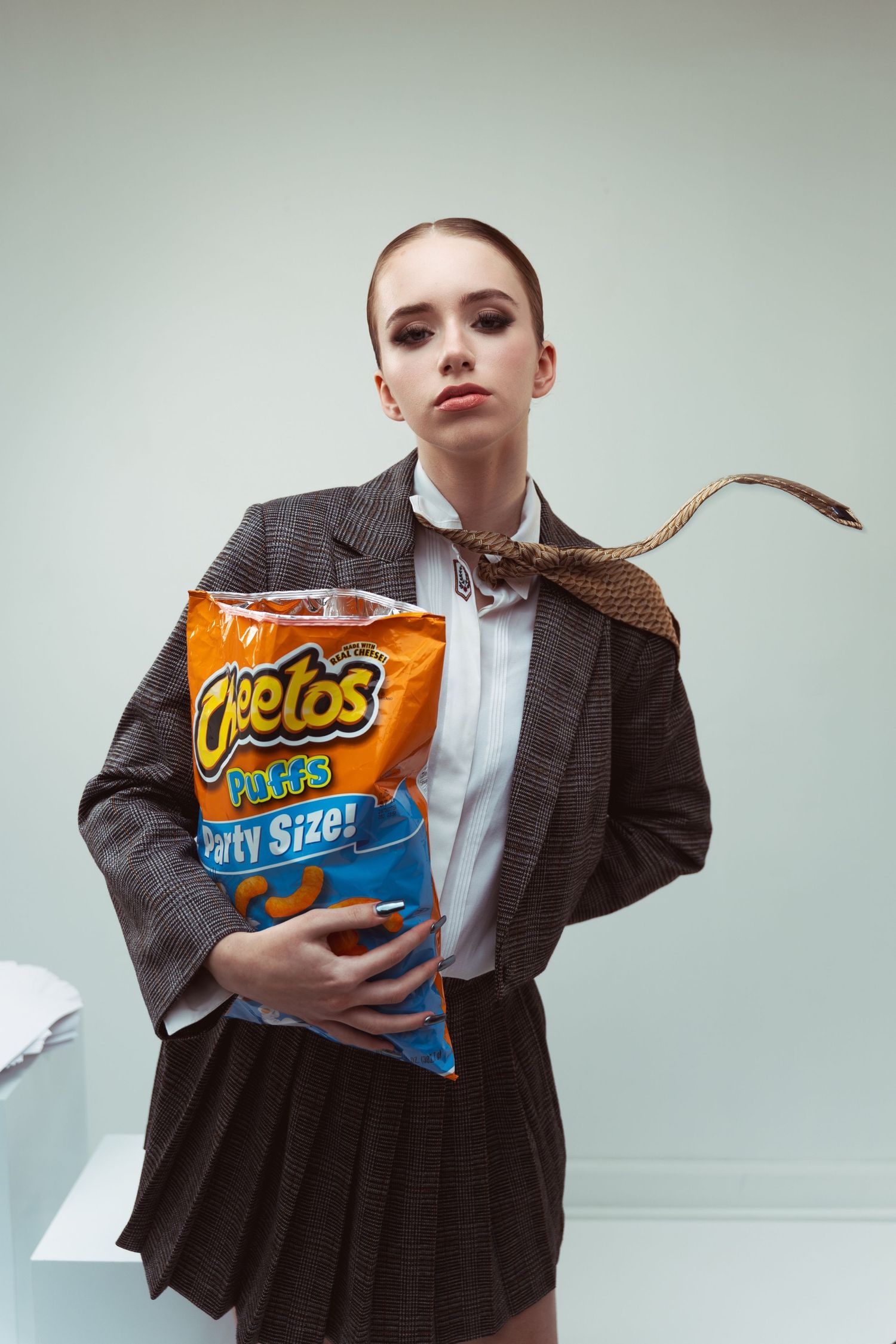 A figure in a professional gray suit outfit poses with a large party-size bag of Cheetos snacks.