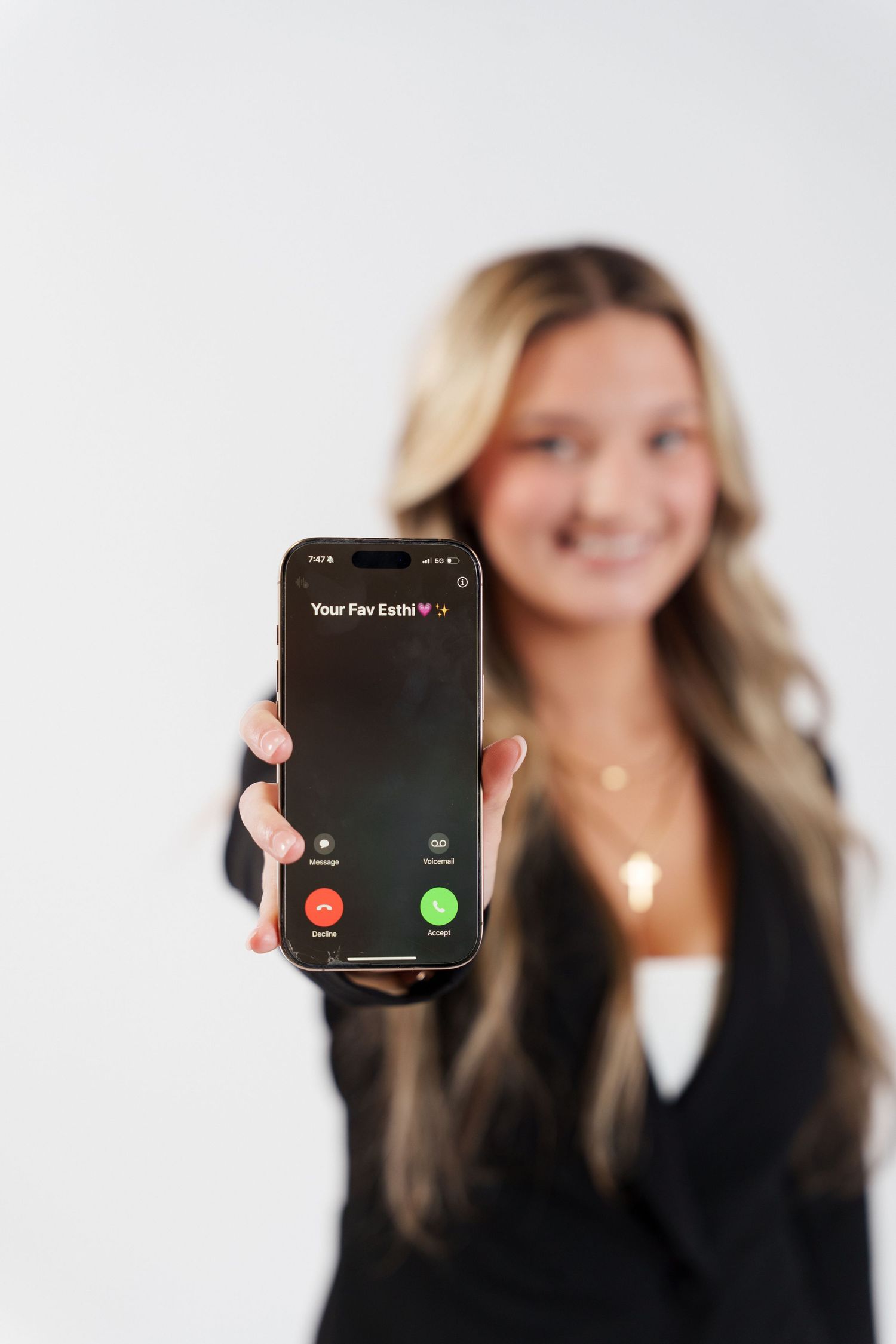 Someone in business attire holding up a phone displaying an incoming call against a white background.