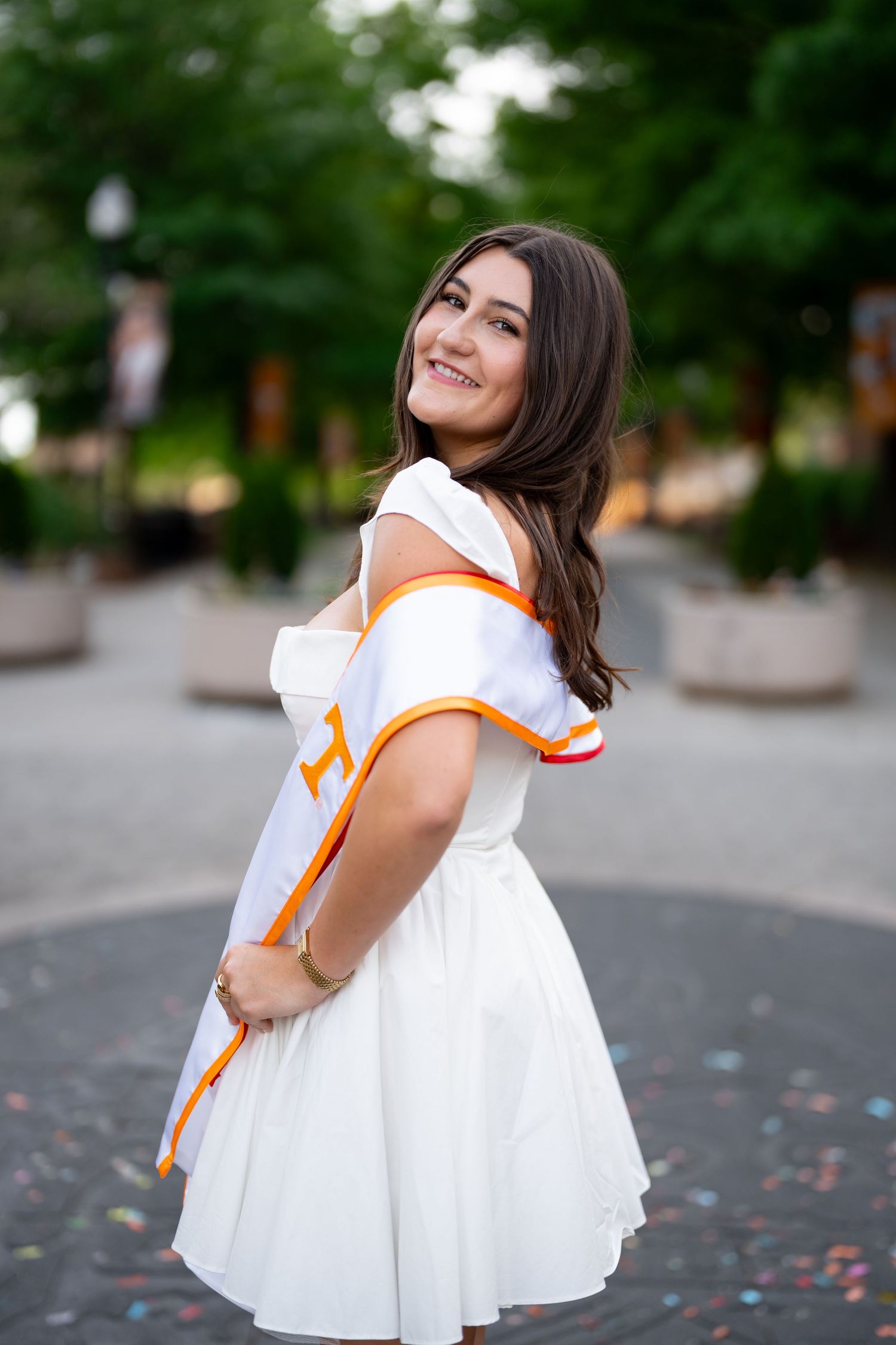 Smiling young woman in white dress with orange trim posing outdoors at University of Tennessee campus.