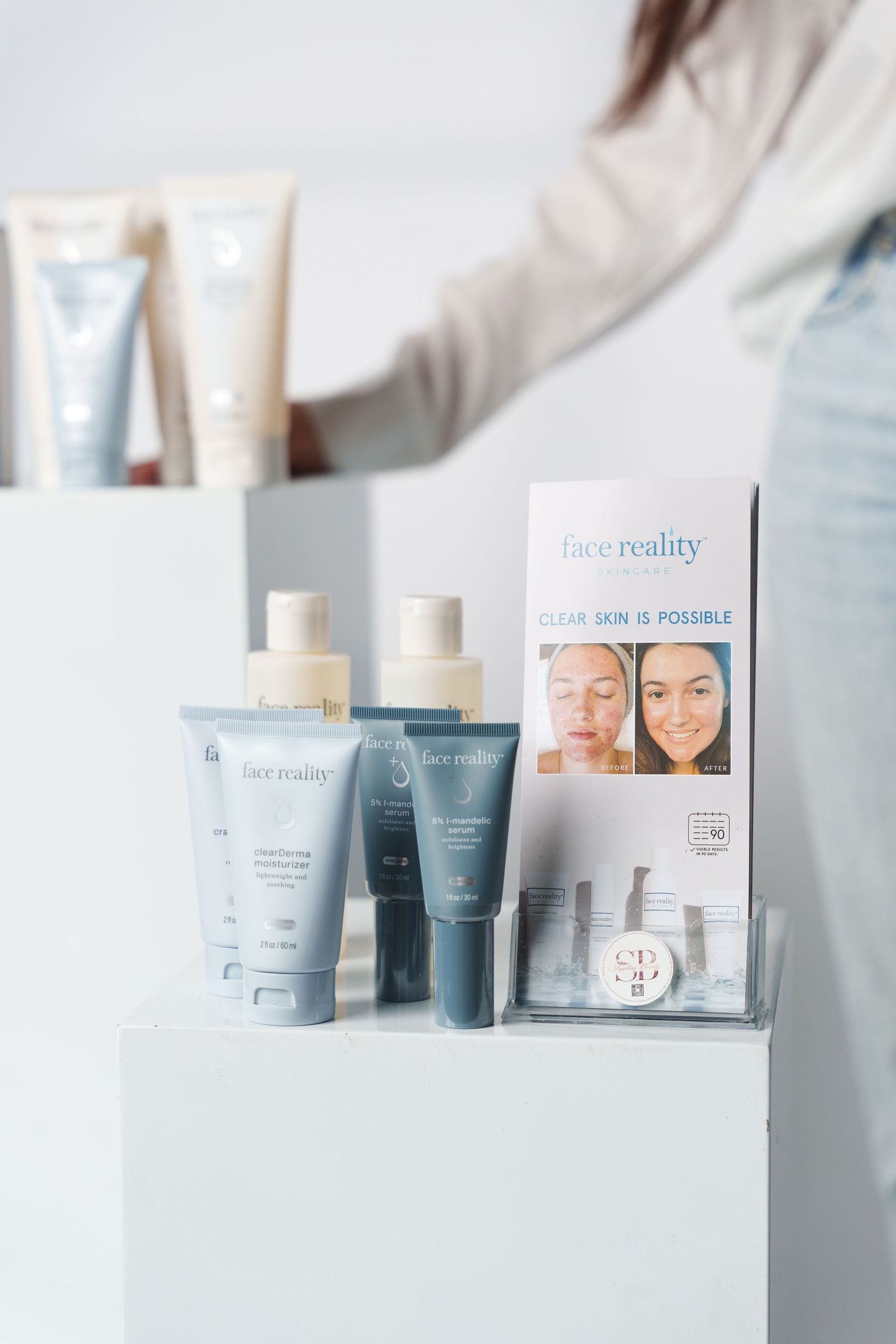 Face Reality skincare products and display stand arranged on white surface with product packaging and tubes in soft lighting.