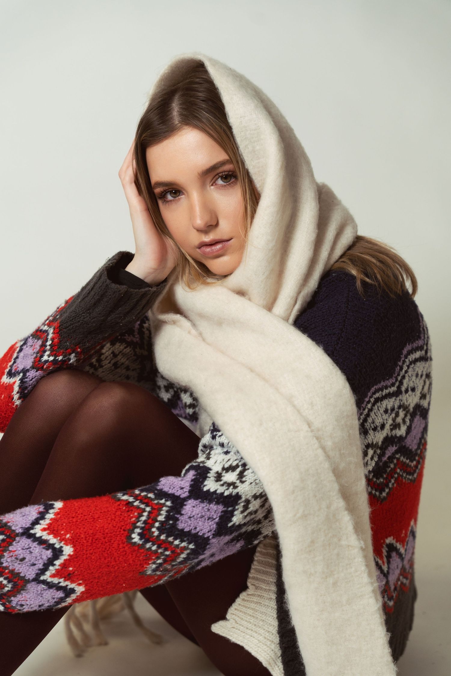 A person wearing a cozy winter outfit with a cream-colored scarf and colorful fair isle patterned sweater in red and navy.