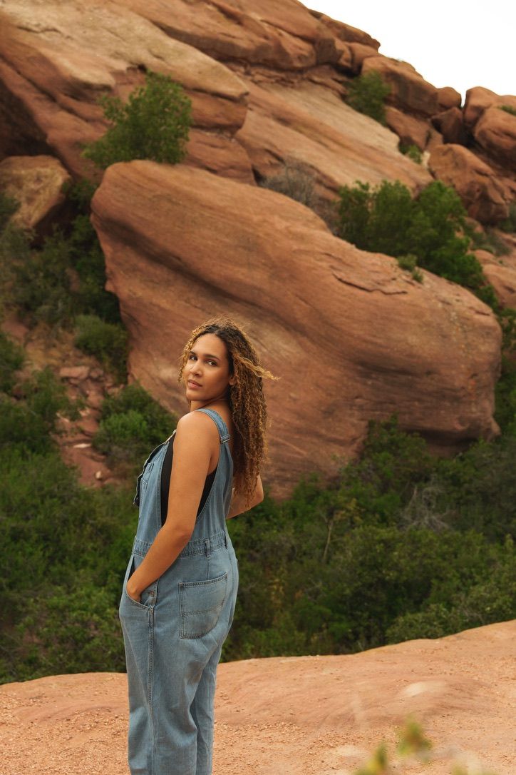 Woman in denim overalls poses against red rock formations at Red Rocks Park, Colorado.