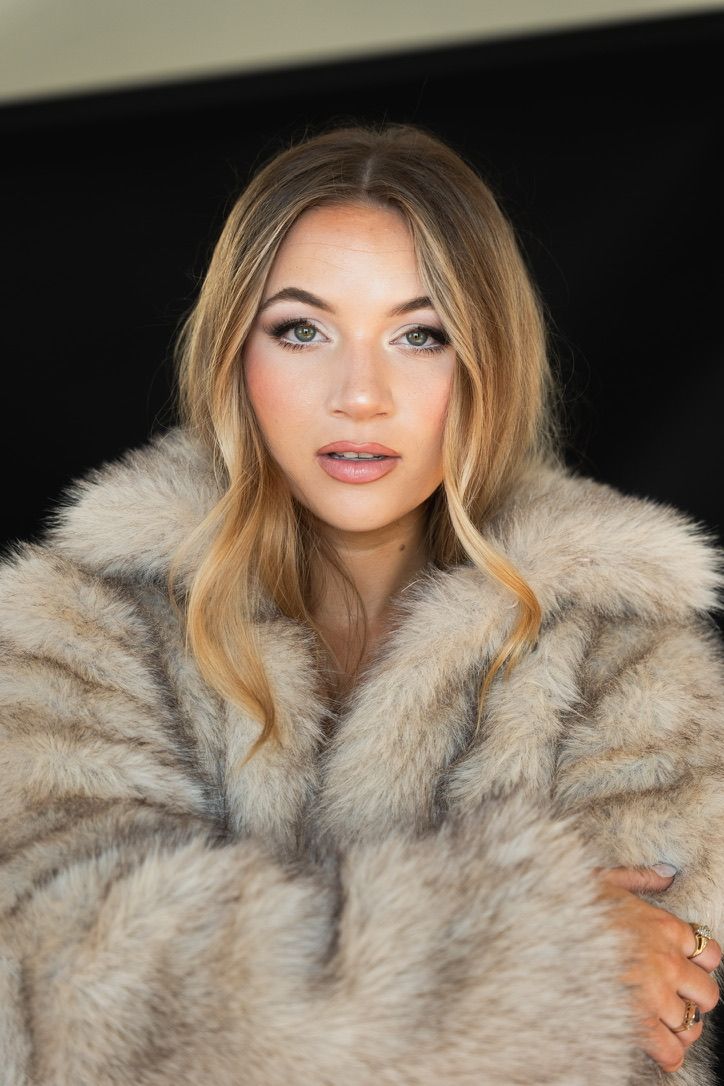 Close-up portrait of woman in beige fur coat against dark background.