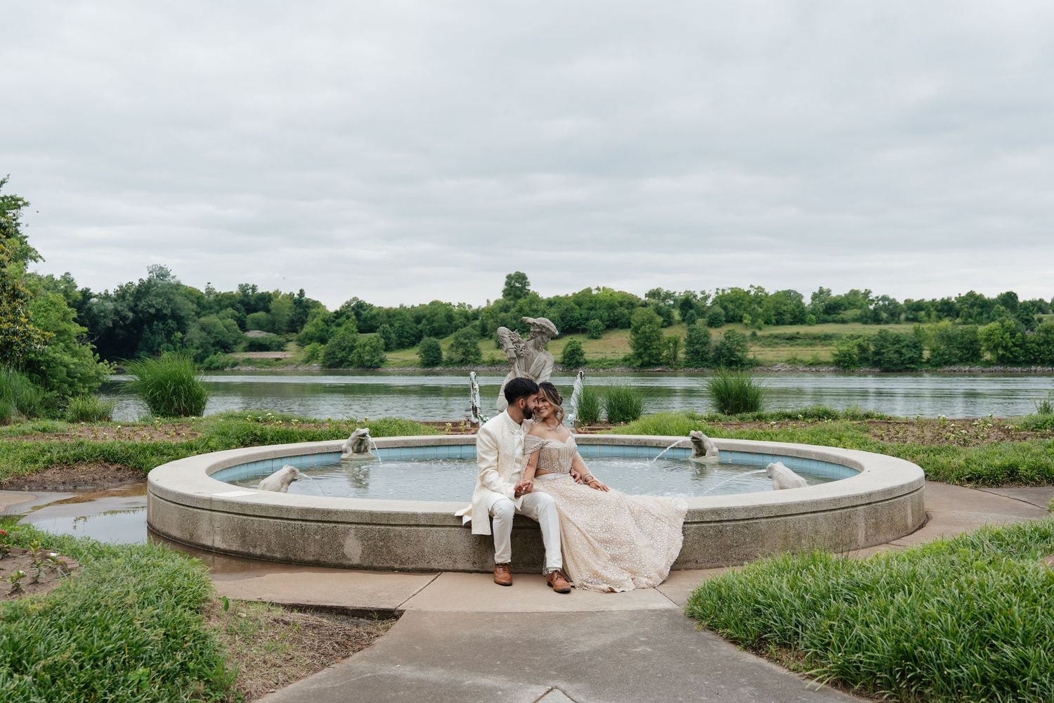 Wedding couple poses at sunset by a curved concrete wall in a garden setting.