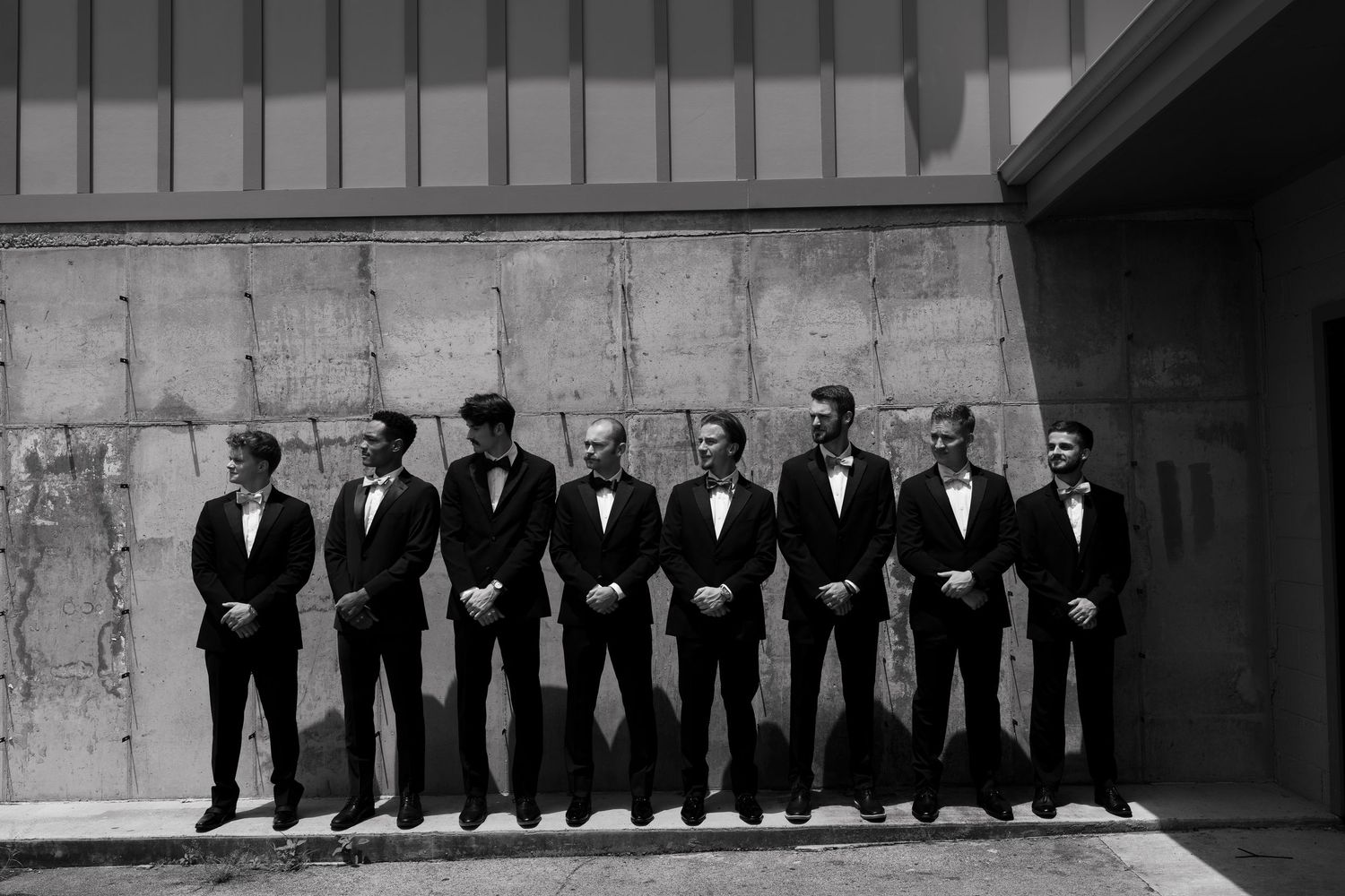 Black and white photo of figures seated on high wall in silhouetted poses which creates a striking geometric pattern.
