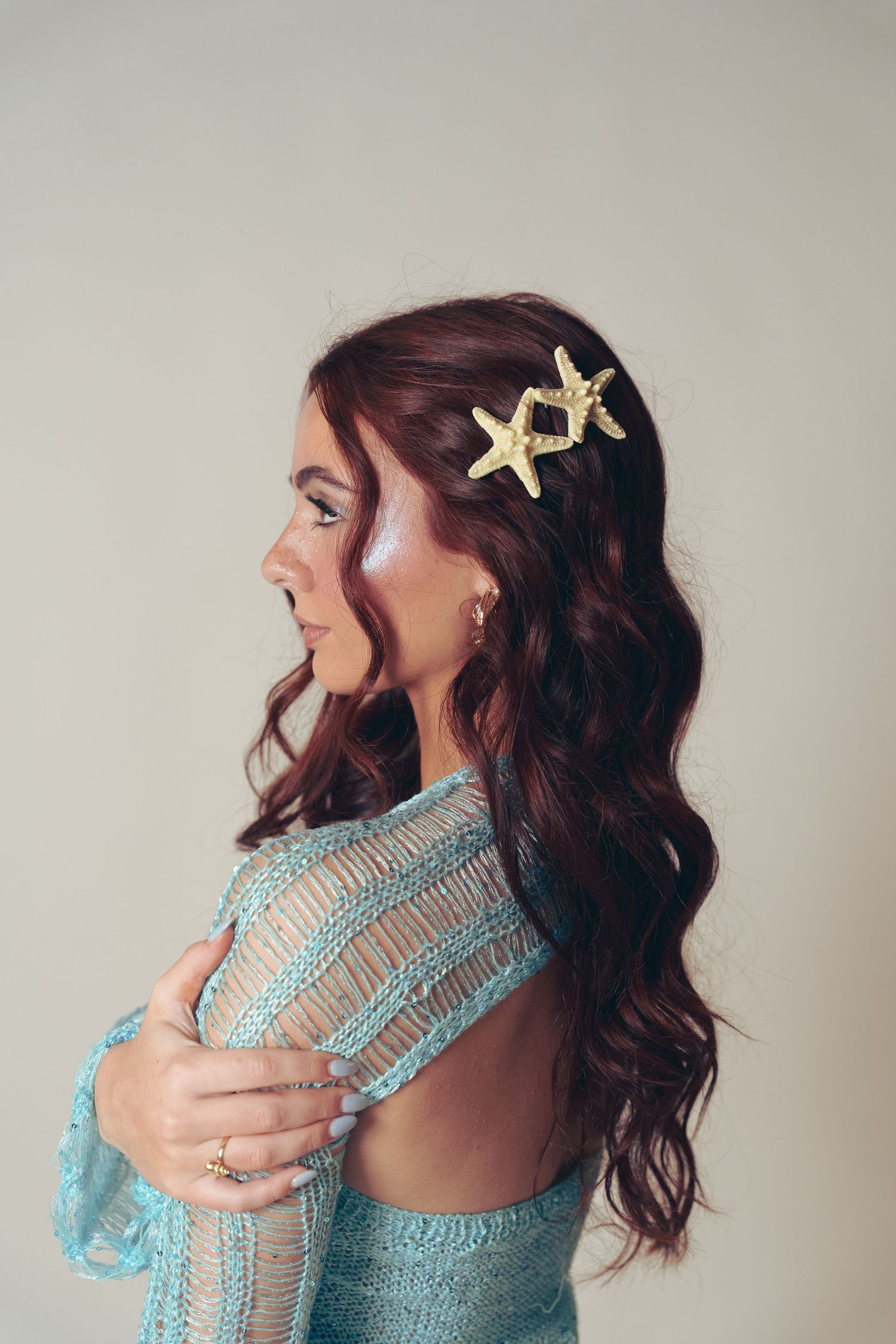 Side profile of brunette in turquoise dress with starfish hair accessories and wavy hair looking away from camera.