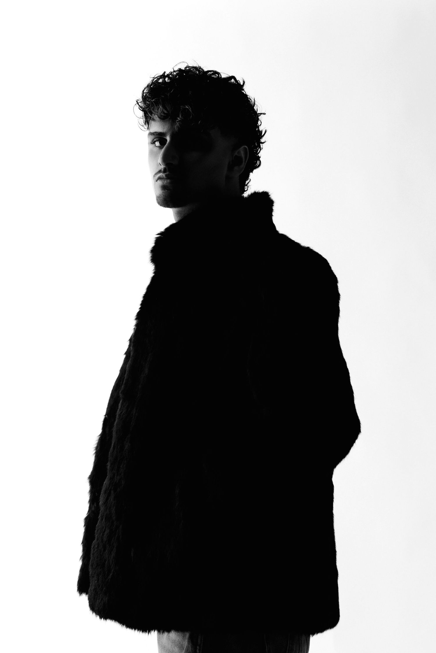 Silhouetted figure in a thick coat creates a dramatic profile against a white background in a black and white photo.