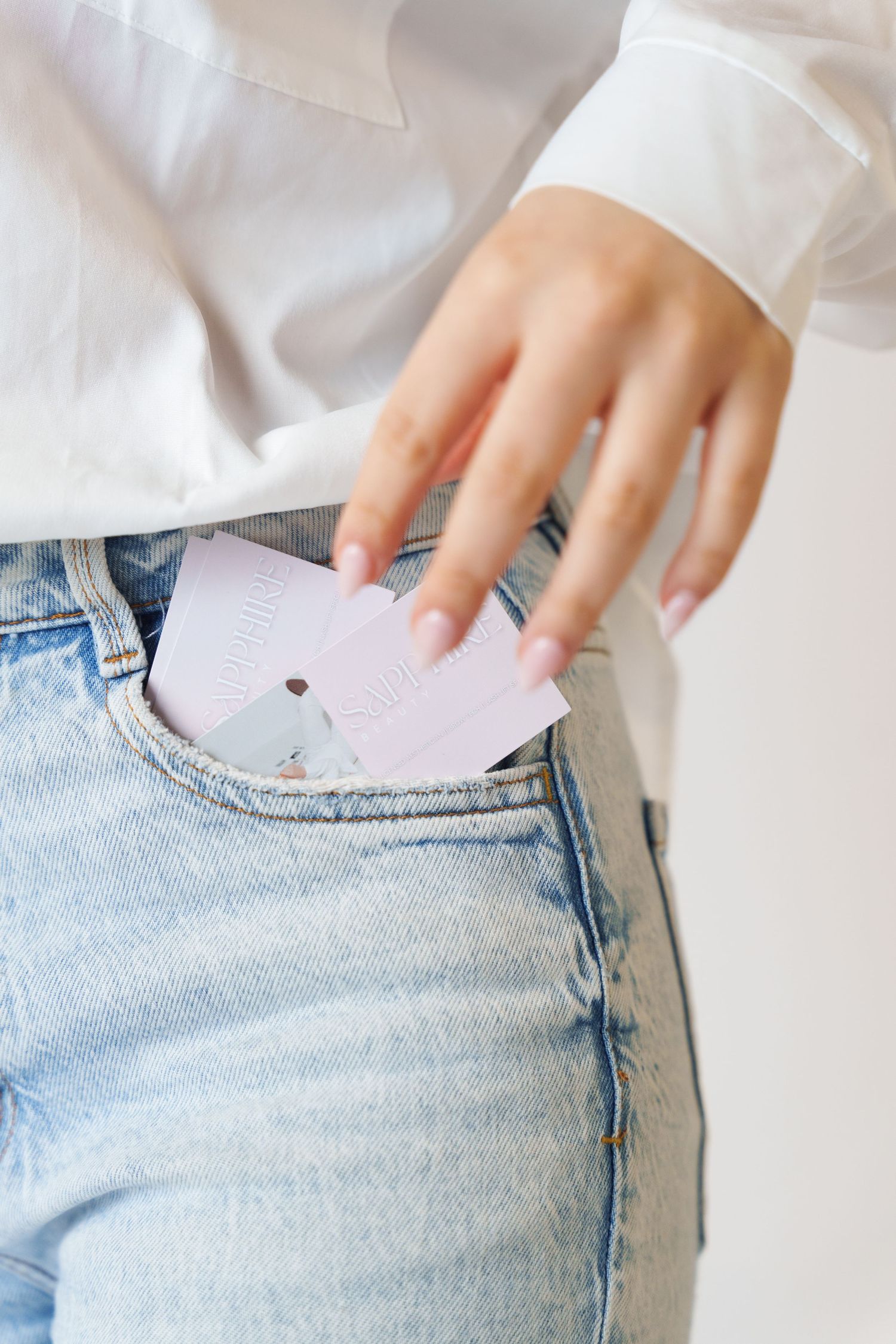 Hand in white sleeve placing a lavender card into the front pocket of light wash denim jeans.