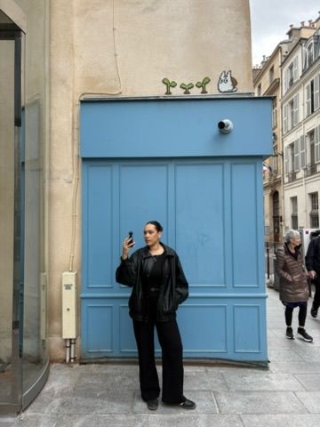 Woman in black outfit standing by a blue door in Paris, with Totoro street art above.